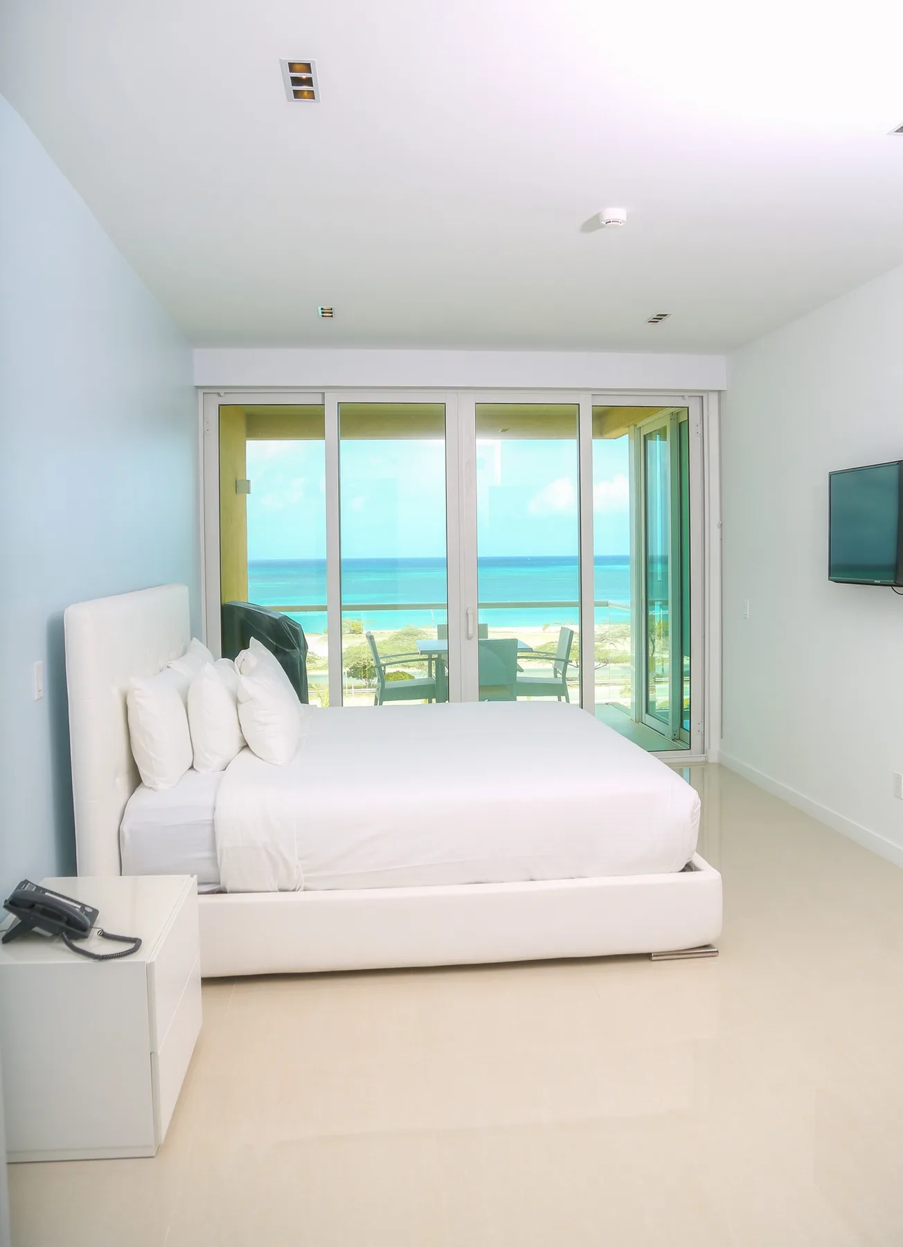 Wake up to crystal-clear turquoise waters framed by floor-to-ceiling glass doors. Your private balcony awaits just beyond this serene, sun-drenched bedroom.