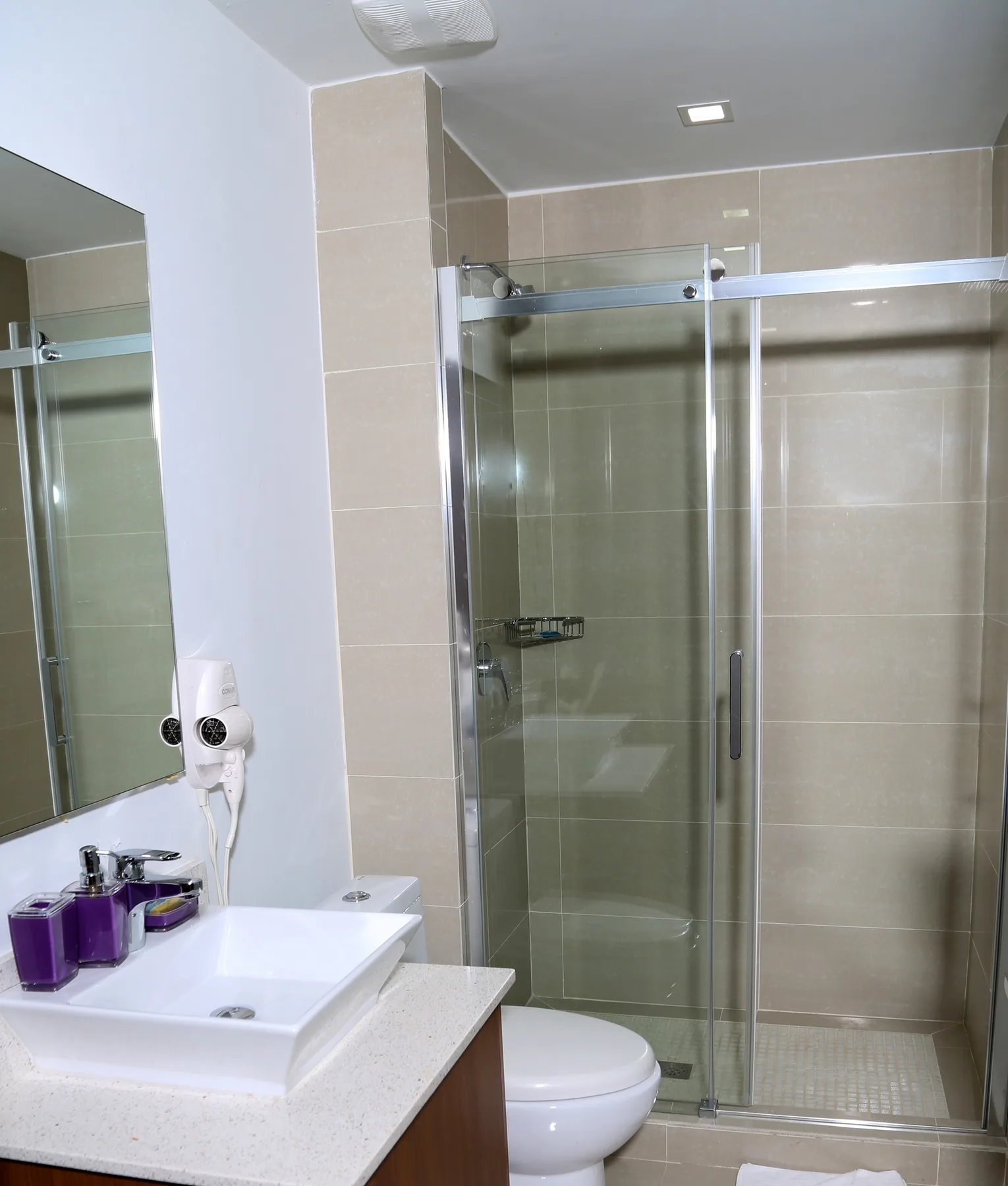 Refresh in your sleek bathroom with modern shower, crisp vanity, and purple amenities adding a vibrant touch to your private retreat.