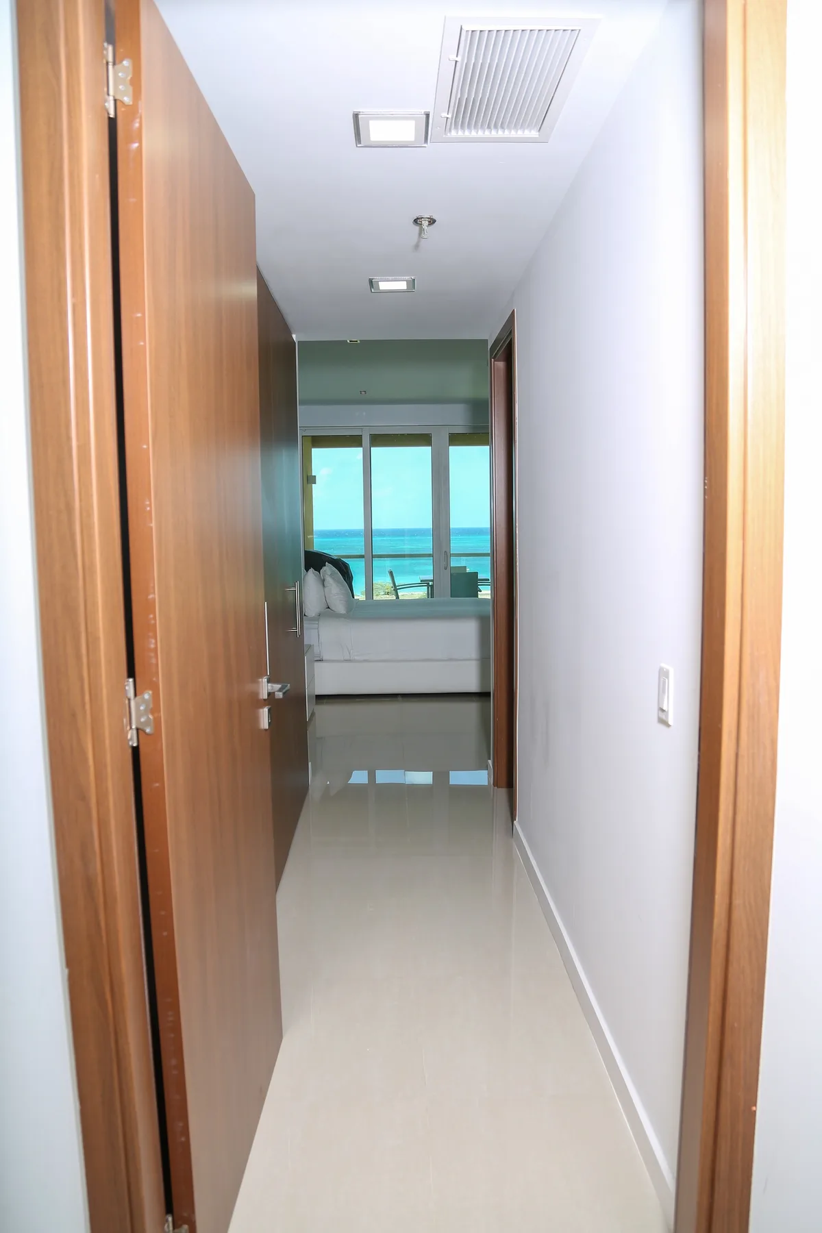 Bright hallway welcomes you with clean lines and stunning ocean views ahead. Natural light flows from the bedroom, where turquoise waters frame your coastal escape.