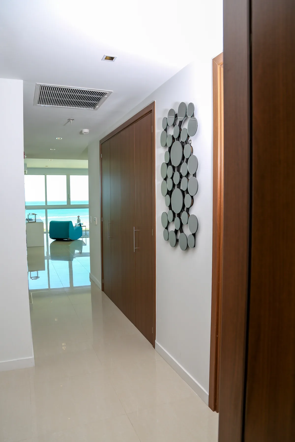 A sleek hallway with modern decor leads you into the bright living area, where stunning ocean views await through floor-to-ceiling windows.