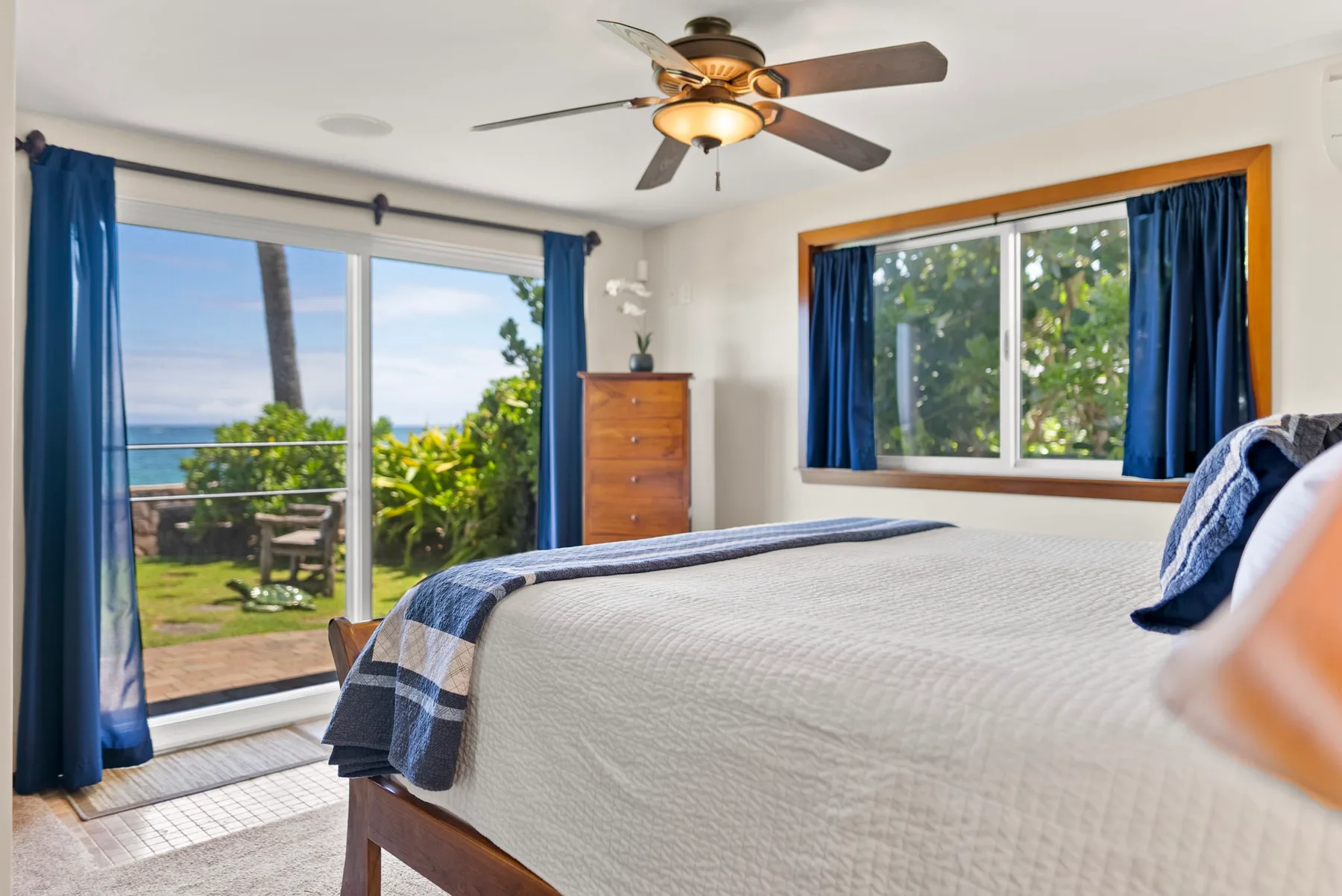 Un dormitorio con una cama, cortinas azules y vistas a la vegetación y al mar.