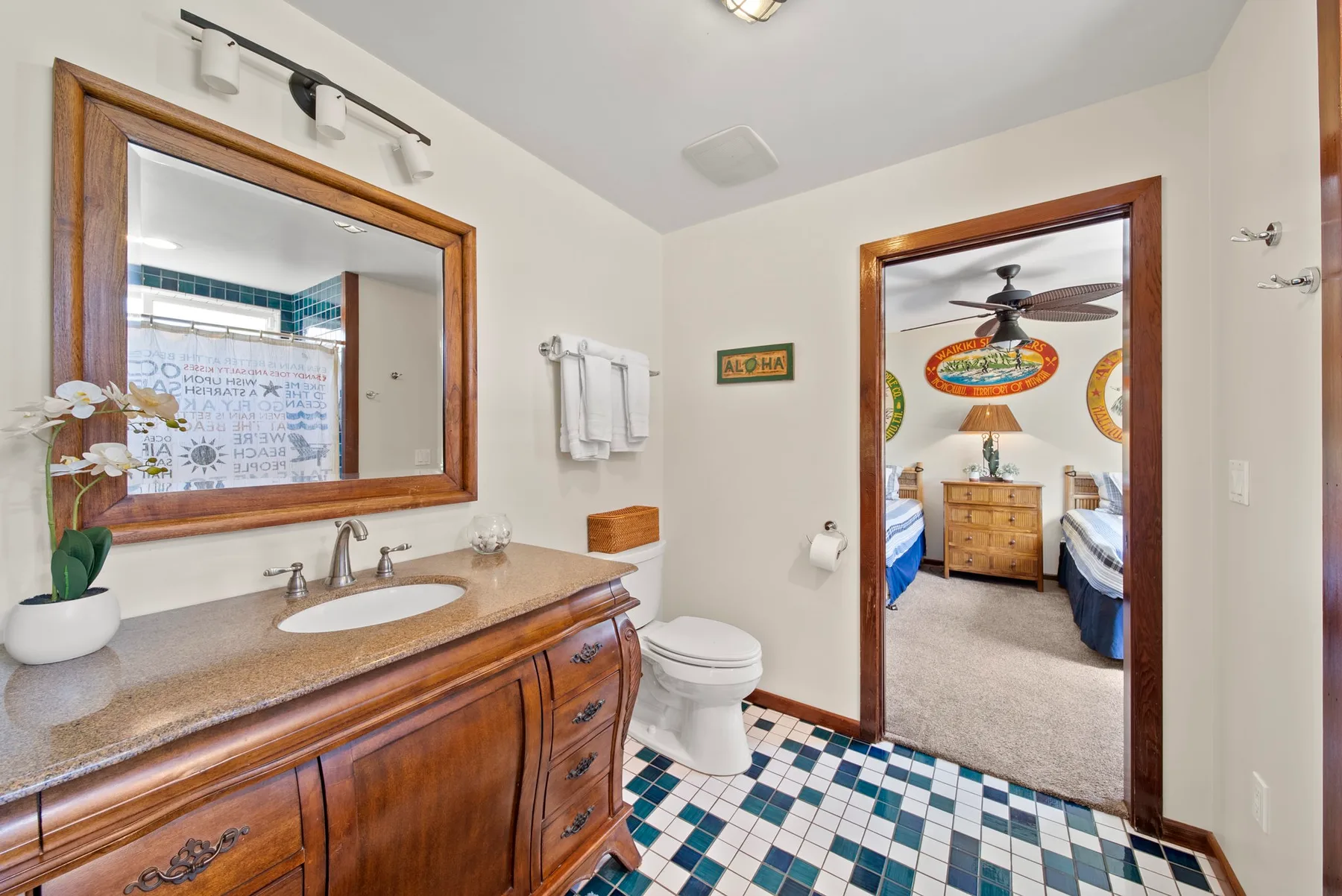 Un baño con tocador de madera, espejo y una puerta hacia un dormitorio.