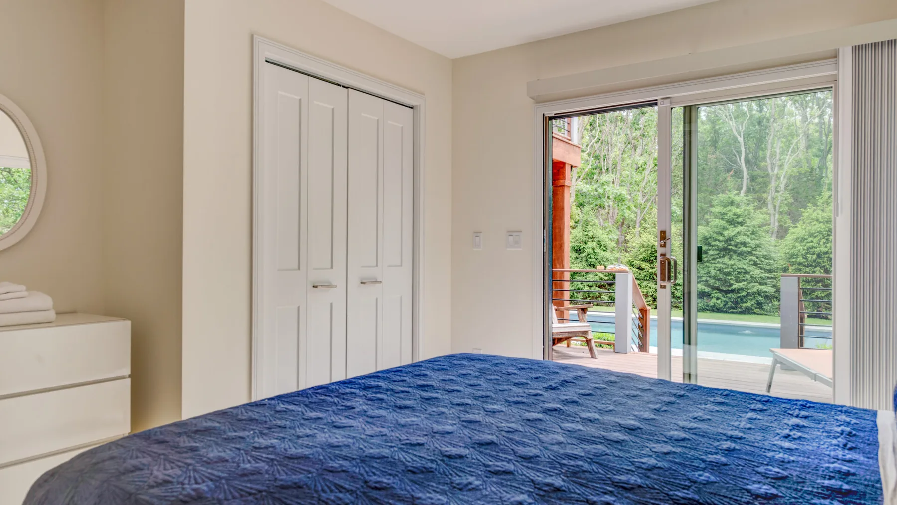 A bedroom with a blue bedspread and sliding glass doors opening onto a patio.