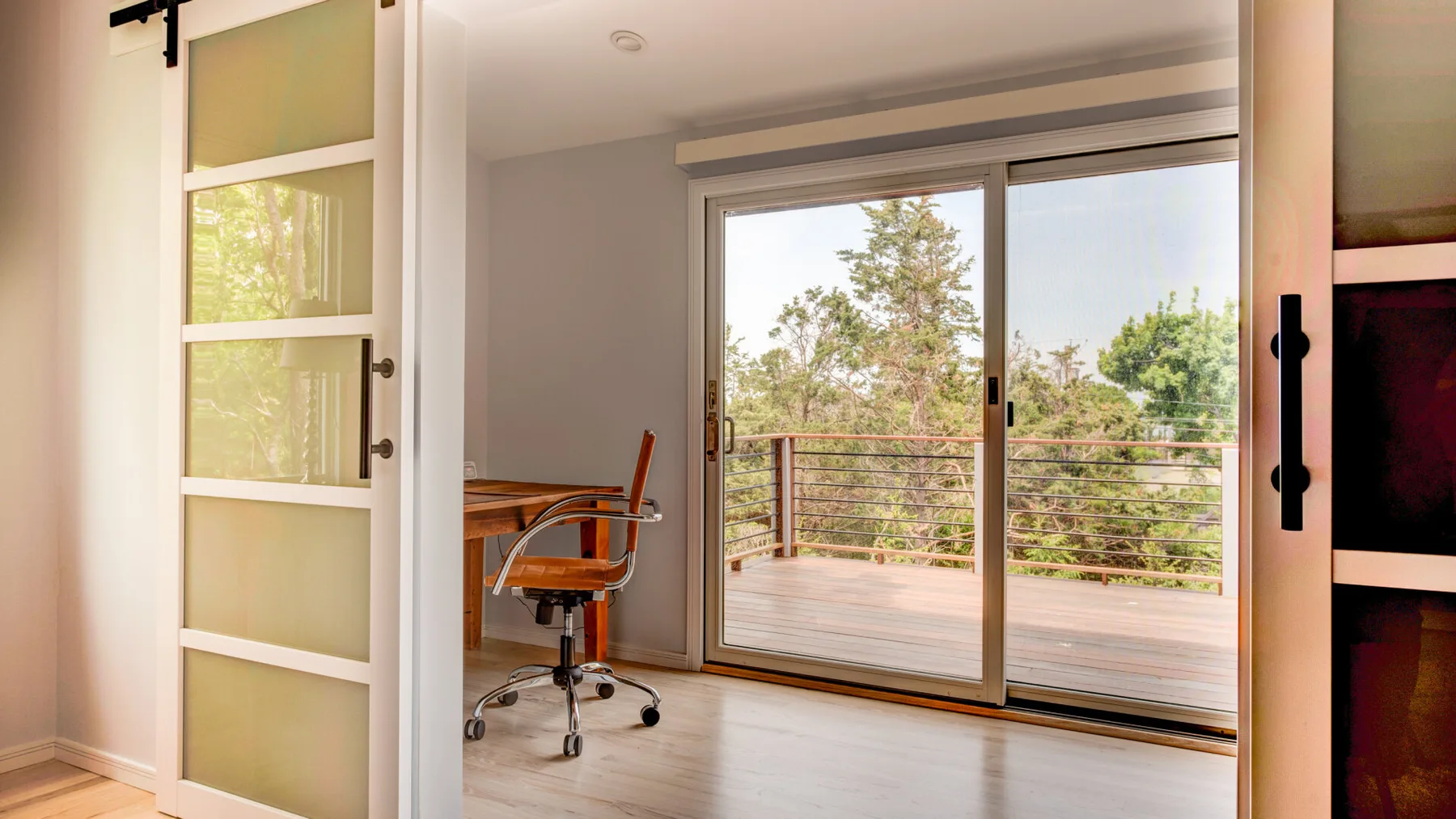 A bright room opens through sliding glass doors onto a balcony with trees beyond.