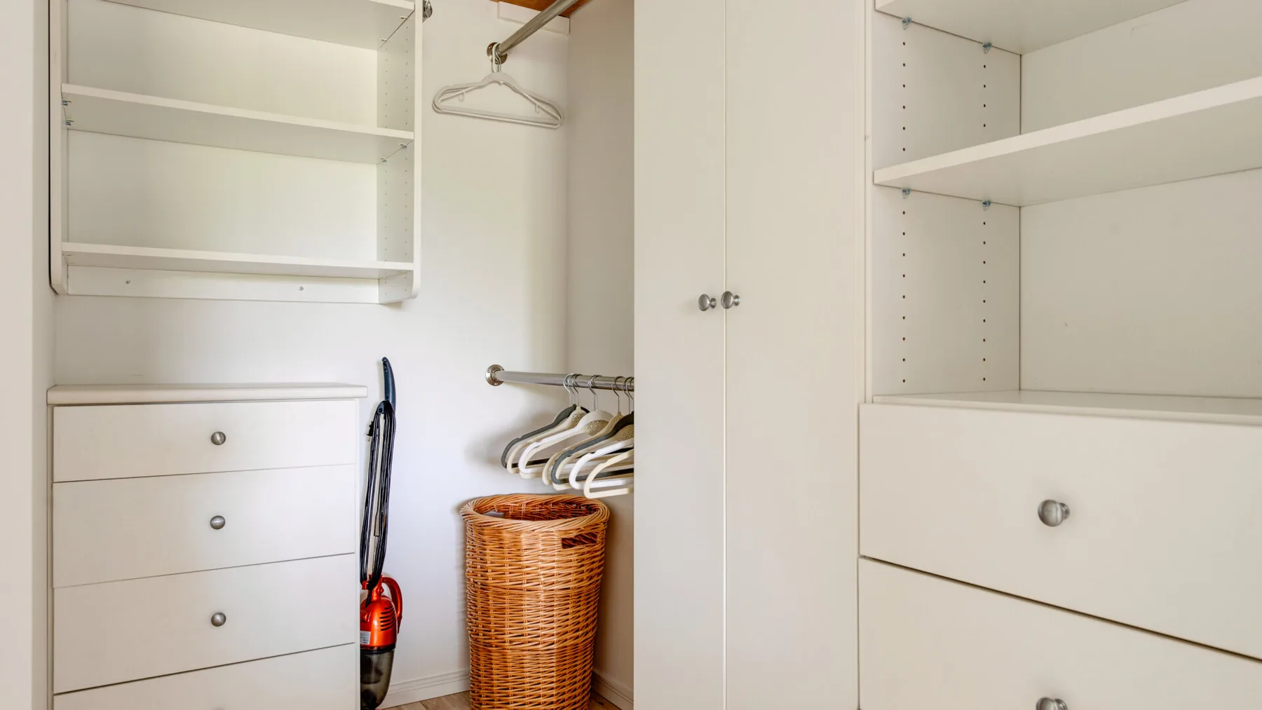 An open closet with shelves, drawers, hangers, and a woven laundry basket.