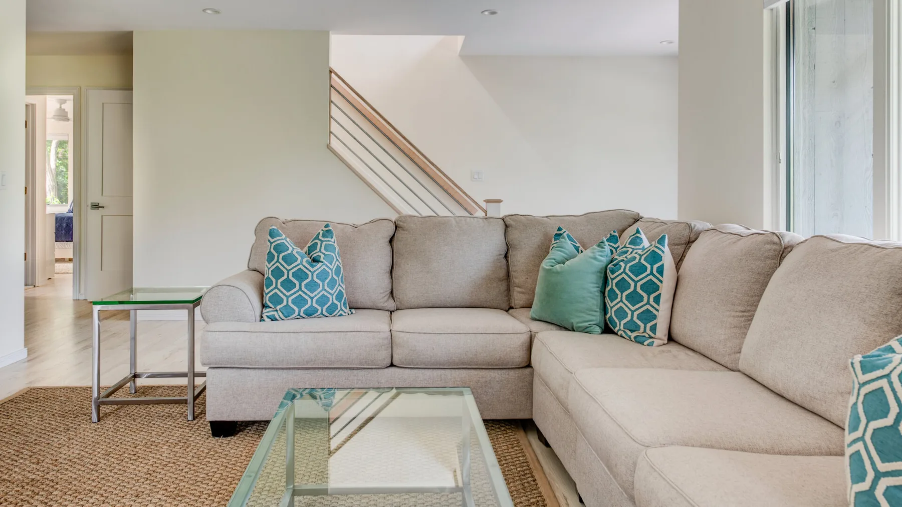 A bright living room with an L-shaped seating area and a glass coffee table.