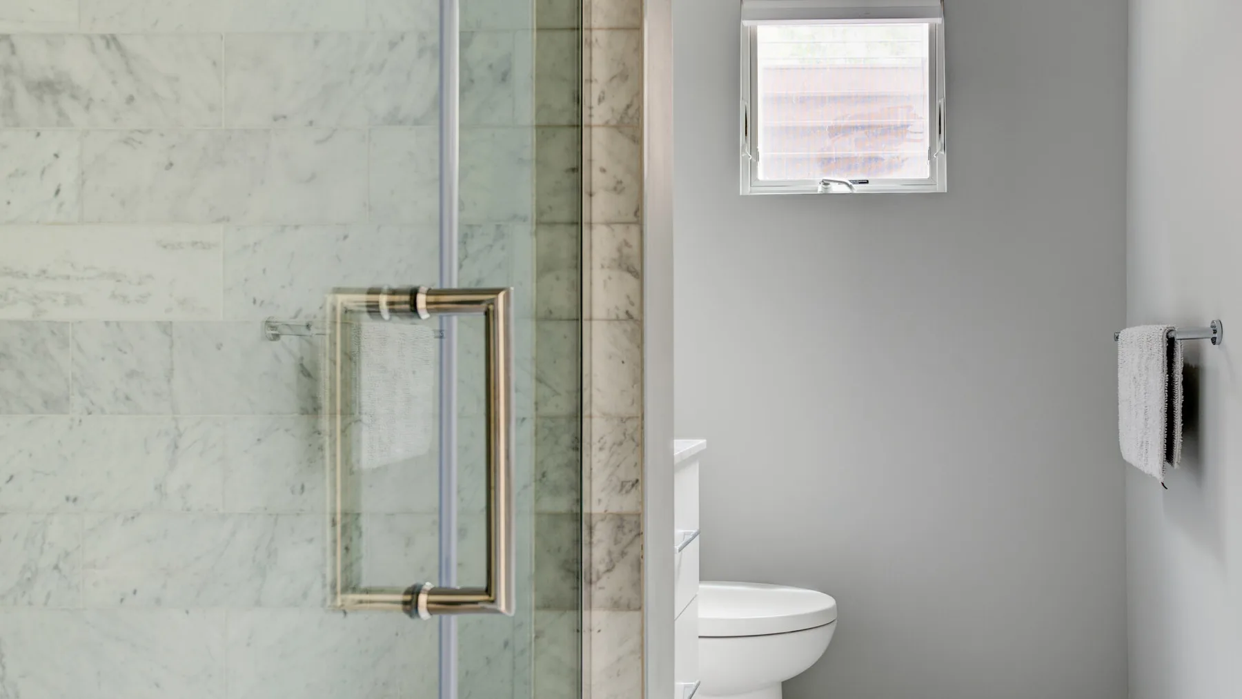 A bathroom with a glass shower enclosure and a small window.