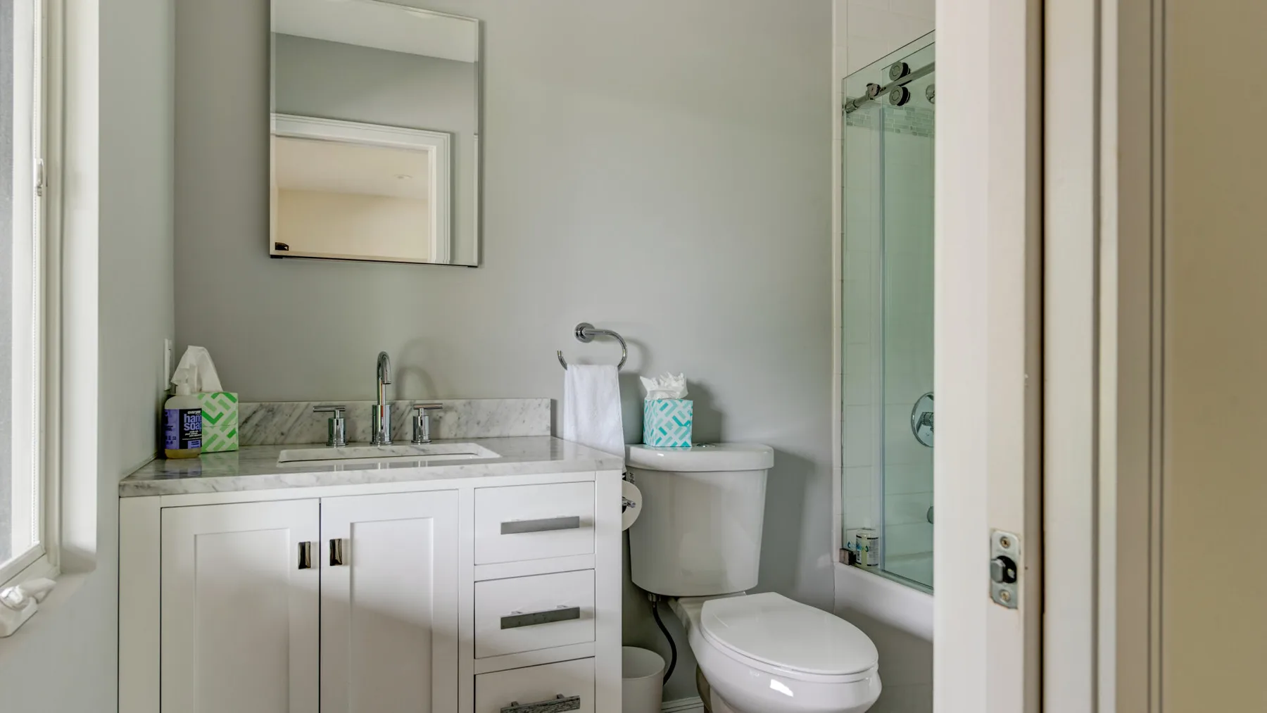 A bathroom with a vanity, mirror, toilet, and glass shower.