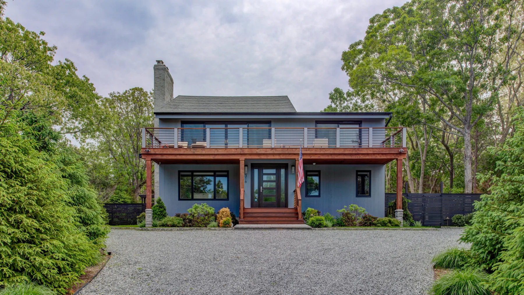 A two-story house with a front porch stands beyond a gravel driveway.