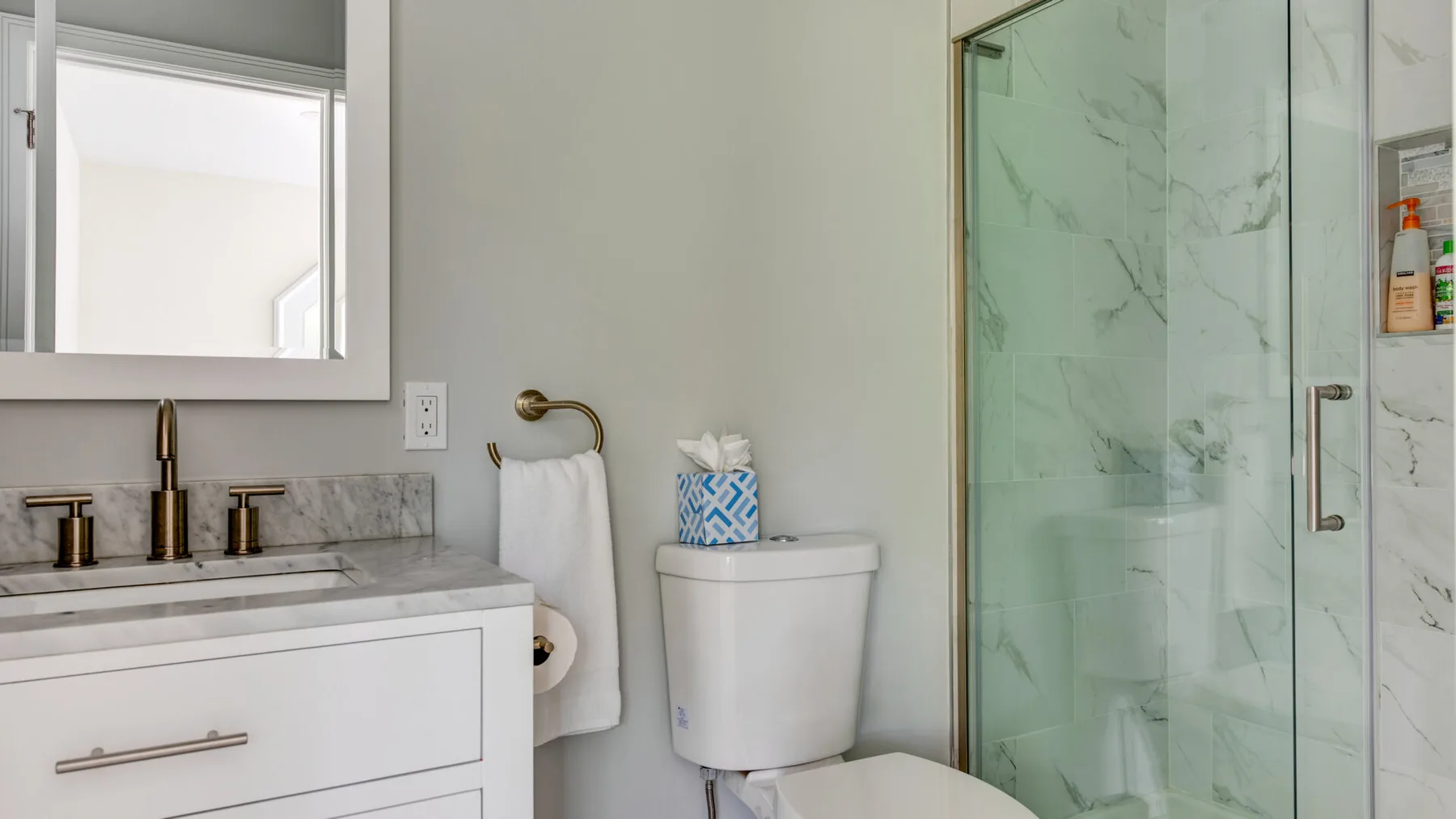 A bathroom with a sink vanity, toilet, and glass-enclosed shower.