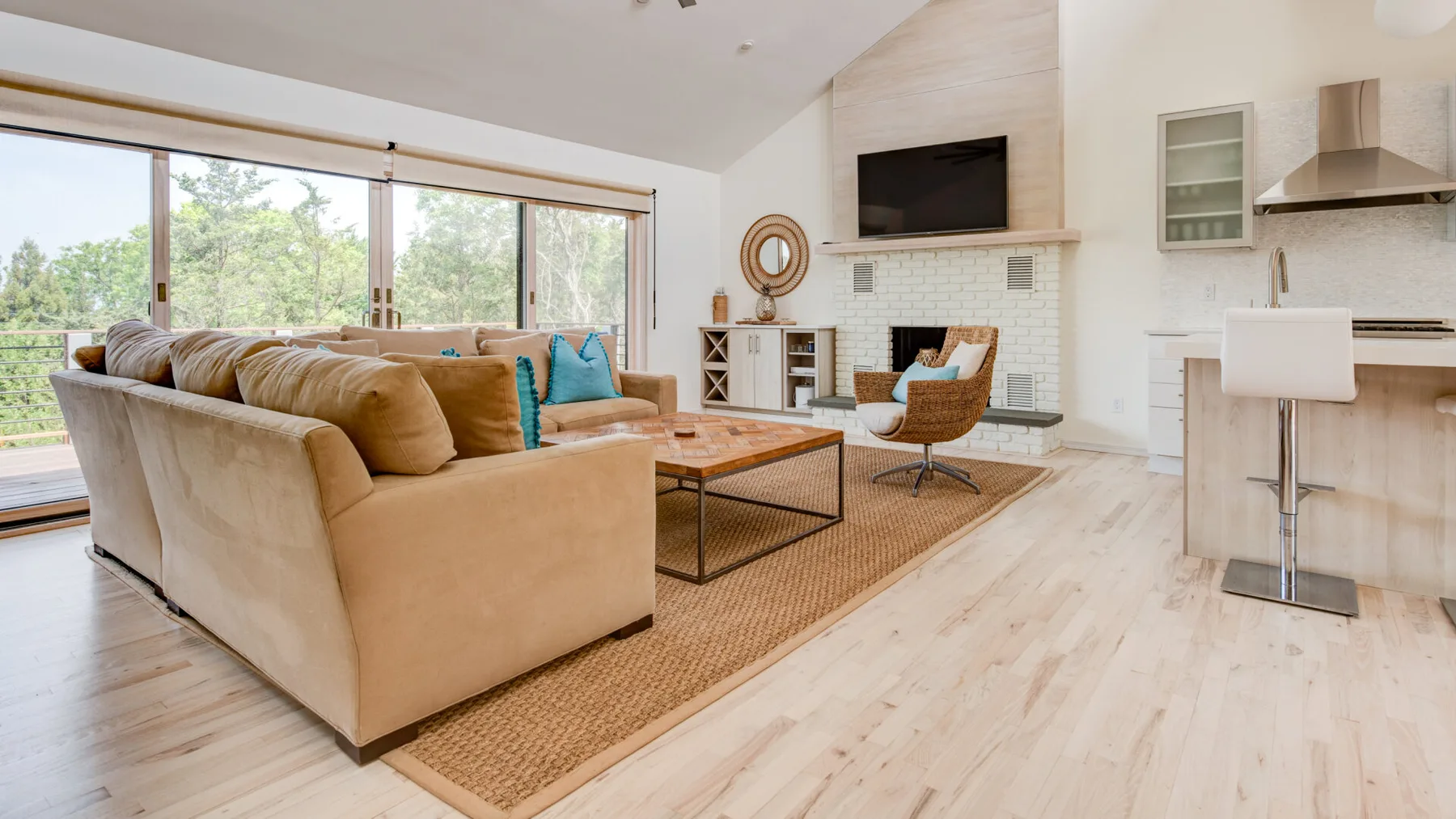 A bright open-plan living room with seating, a television, and large windows.