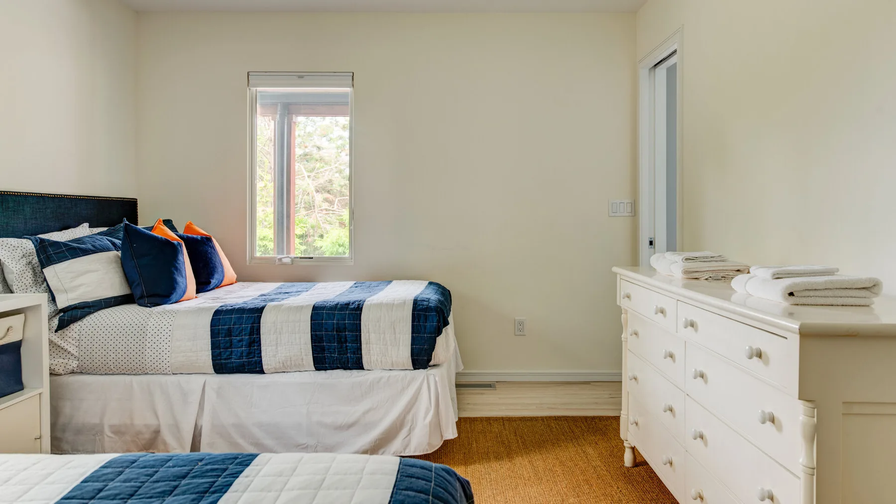A bedroom with a bed dressed in blue and white bedding beside a dresser.