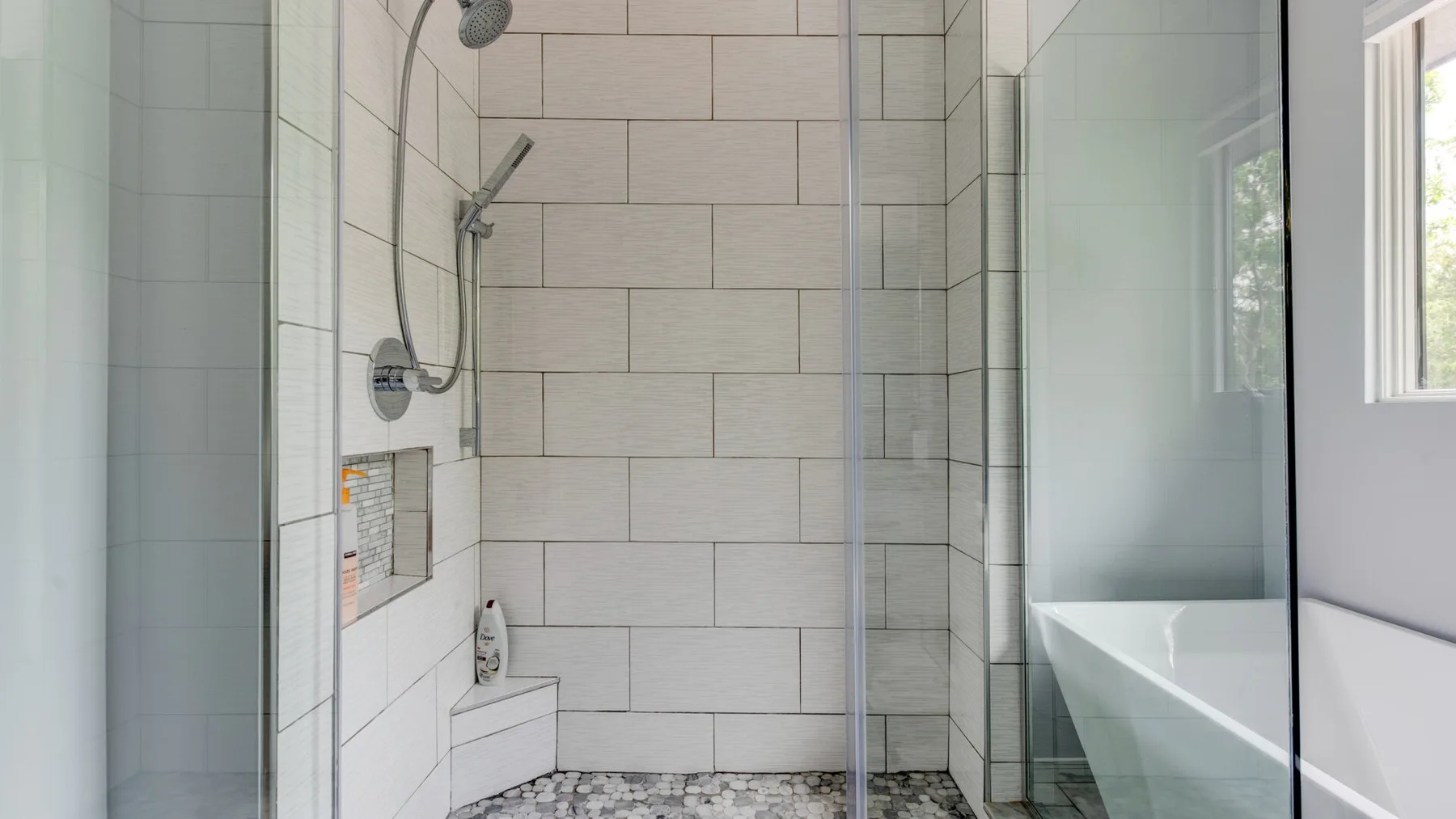 A tiled bathroom with a glass shower and a bathtub beside a window.