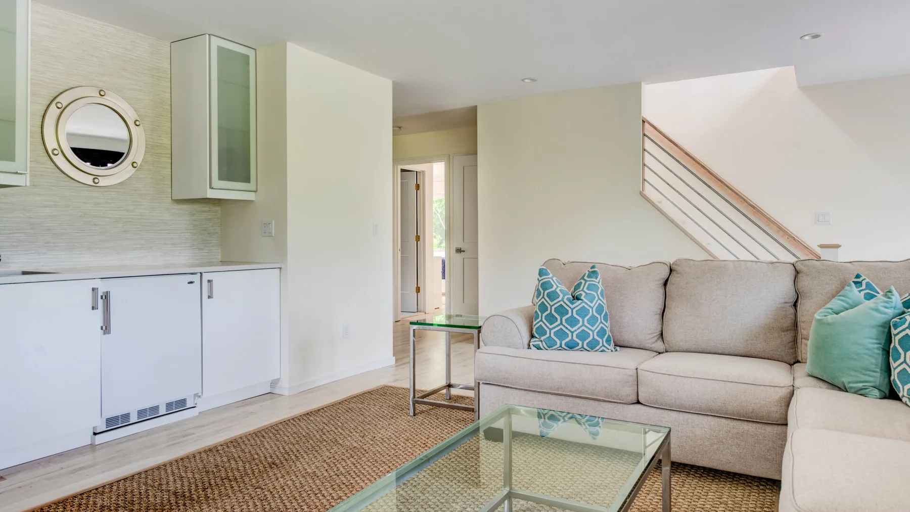 A living room with a sectional sofa, glass coffee table, and staircase.