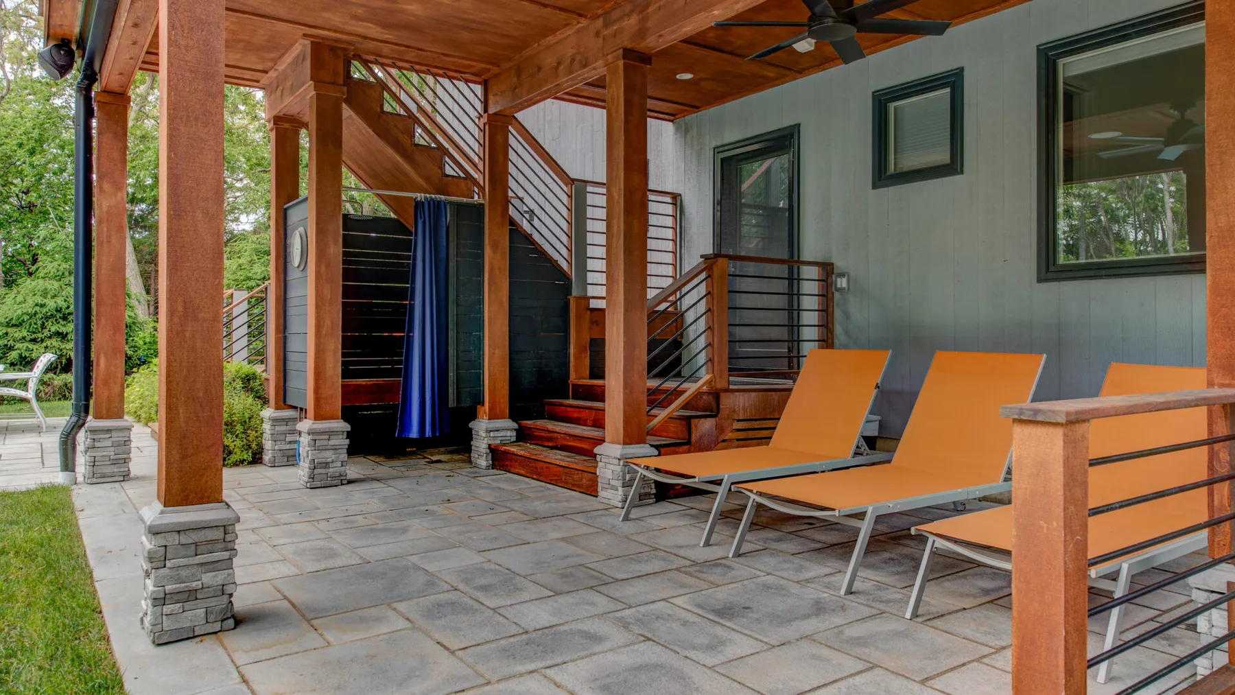 A covered patio with orange lounge chairs and a staircase.