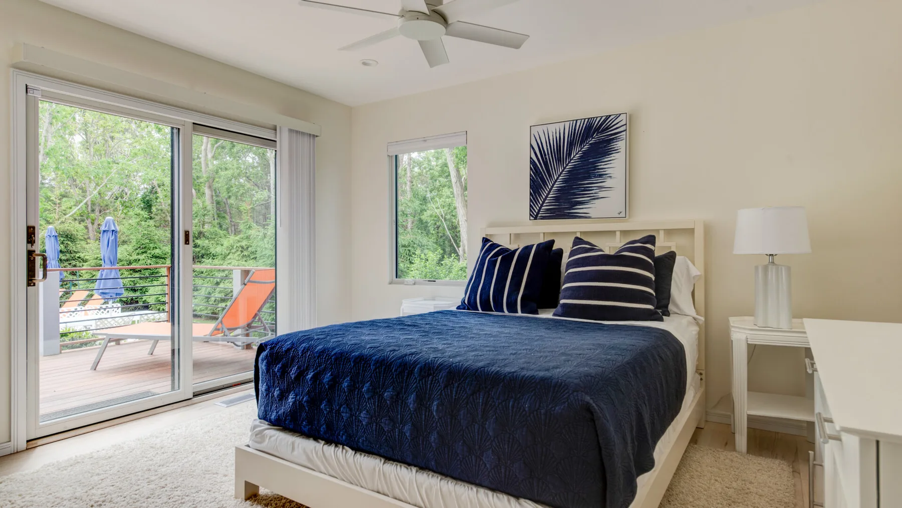 A bedroom with a bed covered in dark blue bedding beside a sliding glass door.