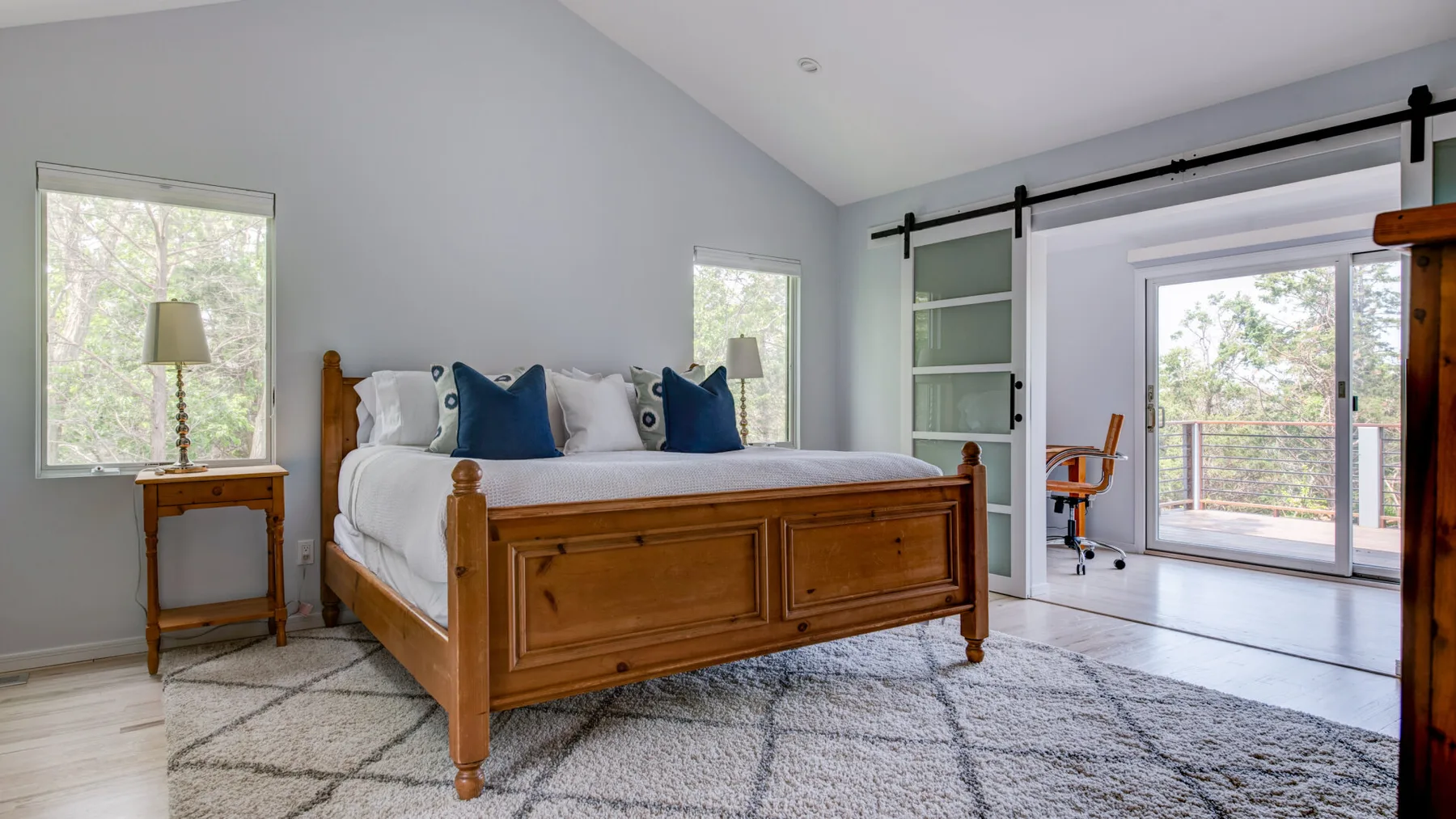 A bright bedroom with a wooden bed, white bedding, and sliding glass doors.