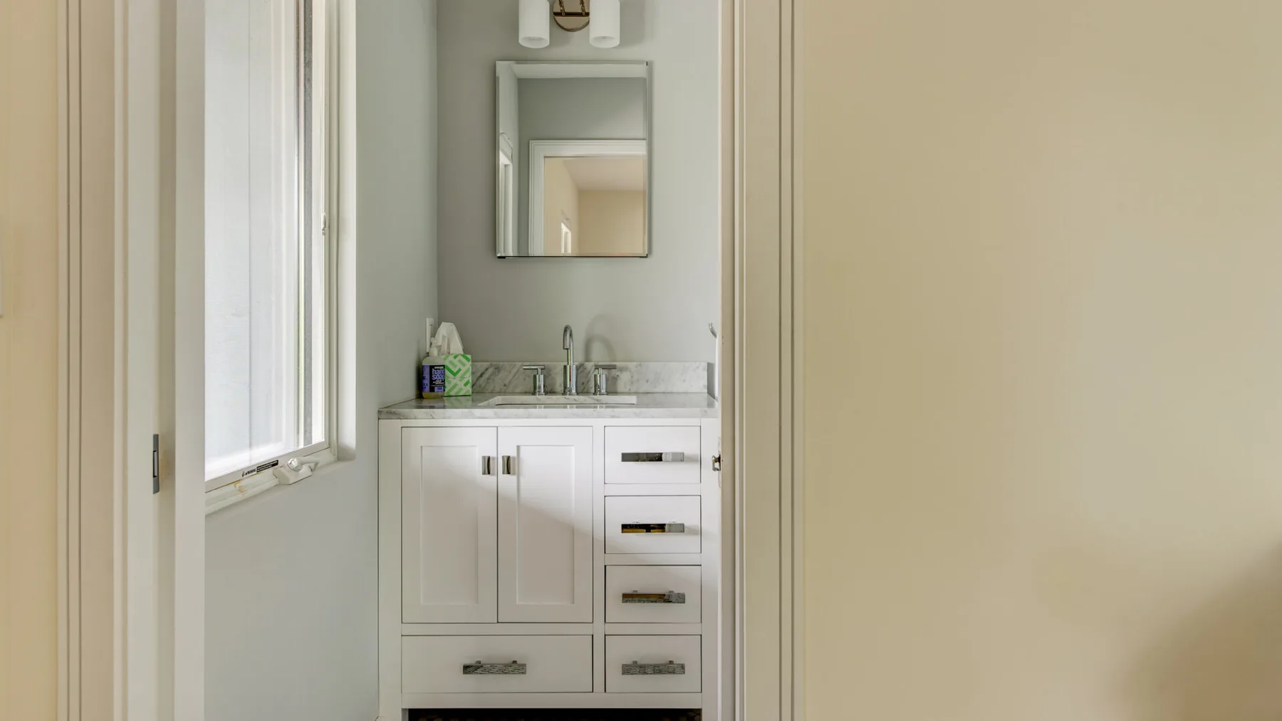 A bathroom vanity with a mirror and bright window.