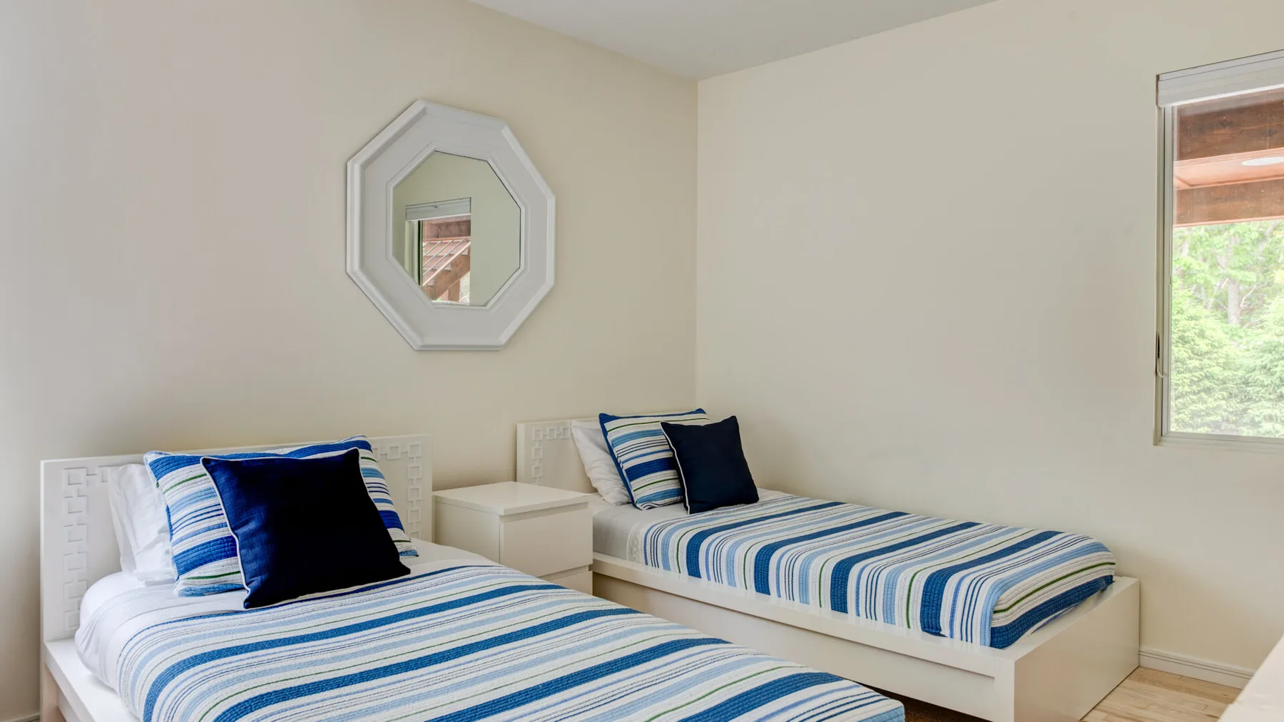 A bright bedroom with two beds dressed in blue and white striped bedding.