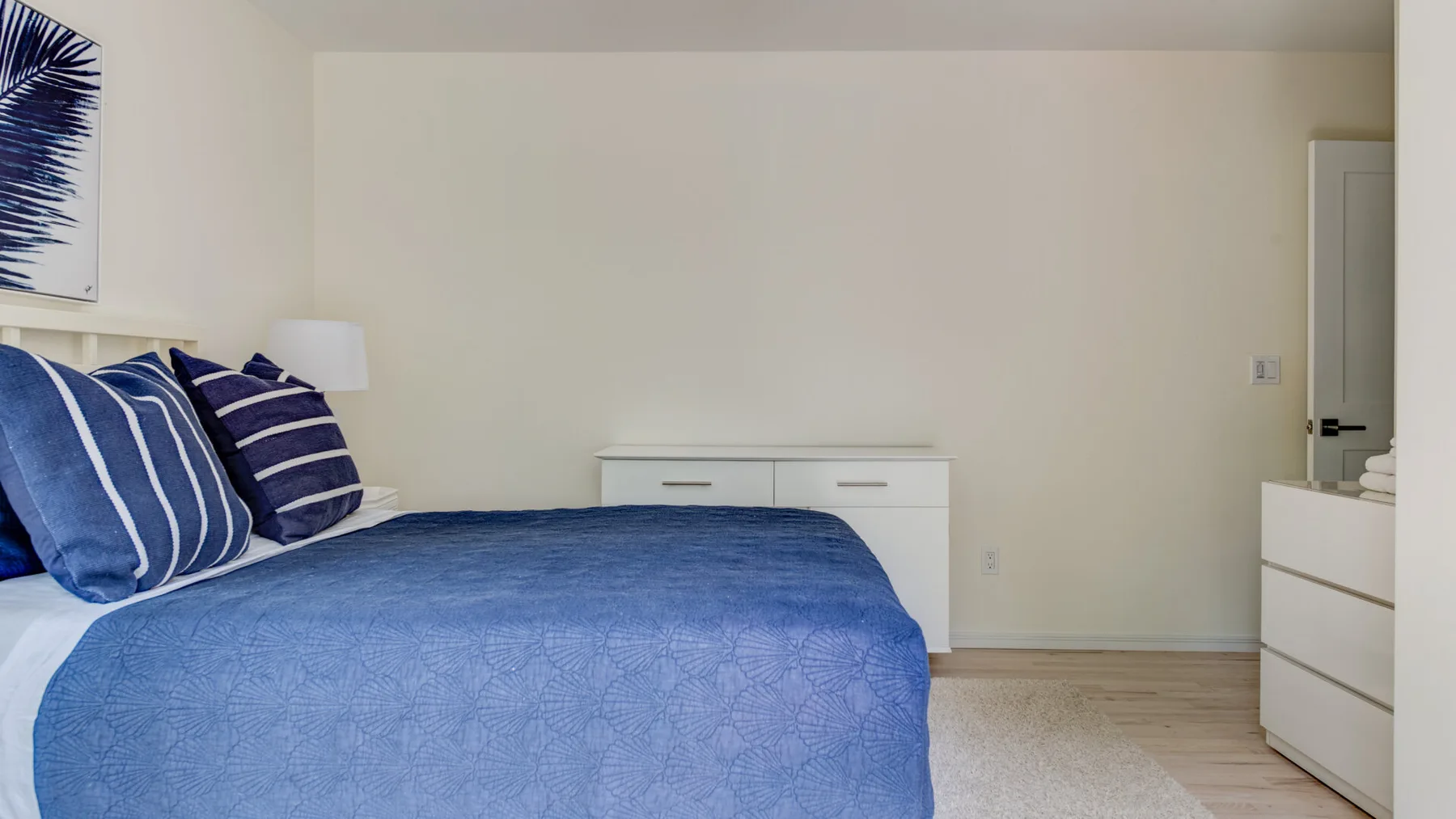A bedroom with blue bedding and a dresser against the wall.