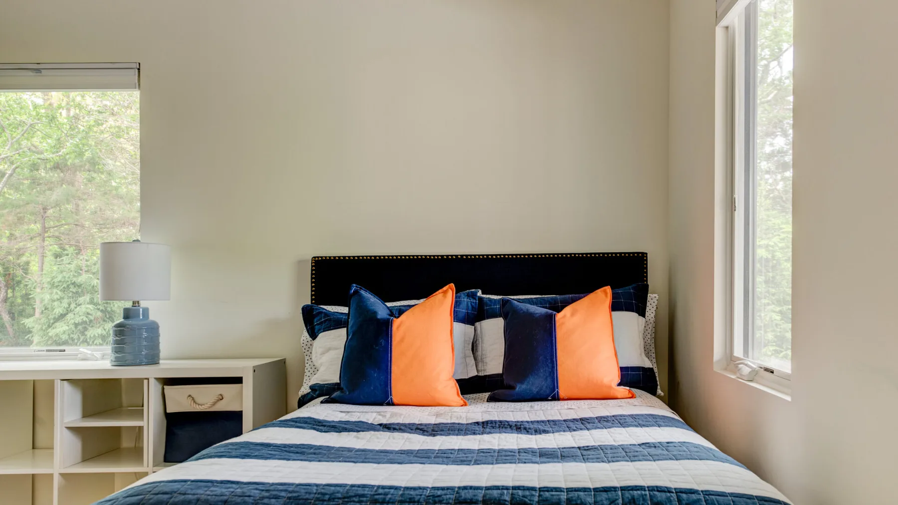 A bedroom with a bed dressed in blue and orange bedding.
