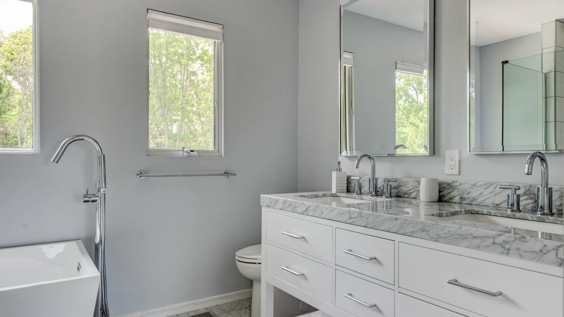 A bright bathroom with a bathtub, vanity, and large mirrors.