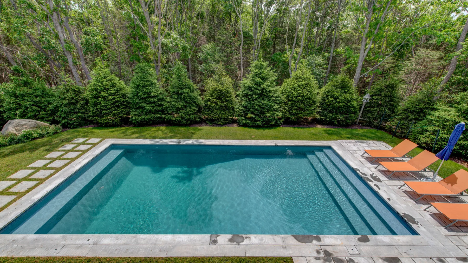 A swimming pool bordered by stone paving and lounge chairs.