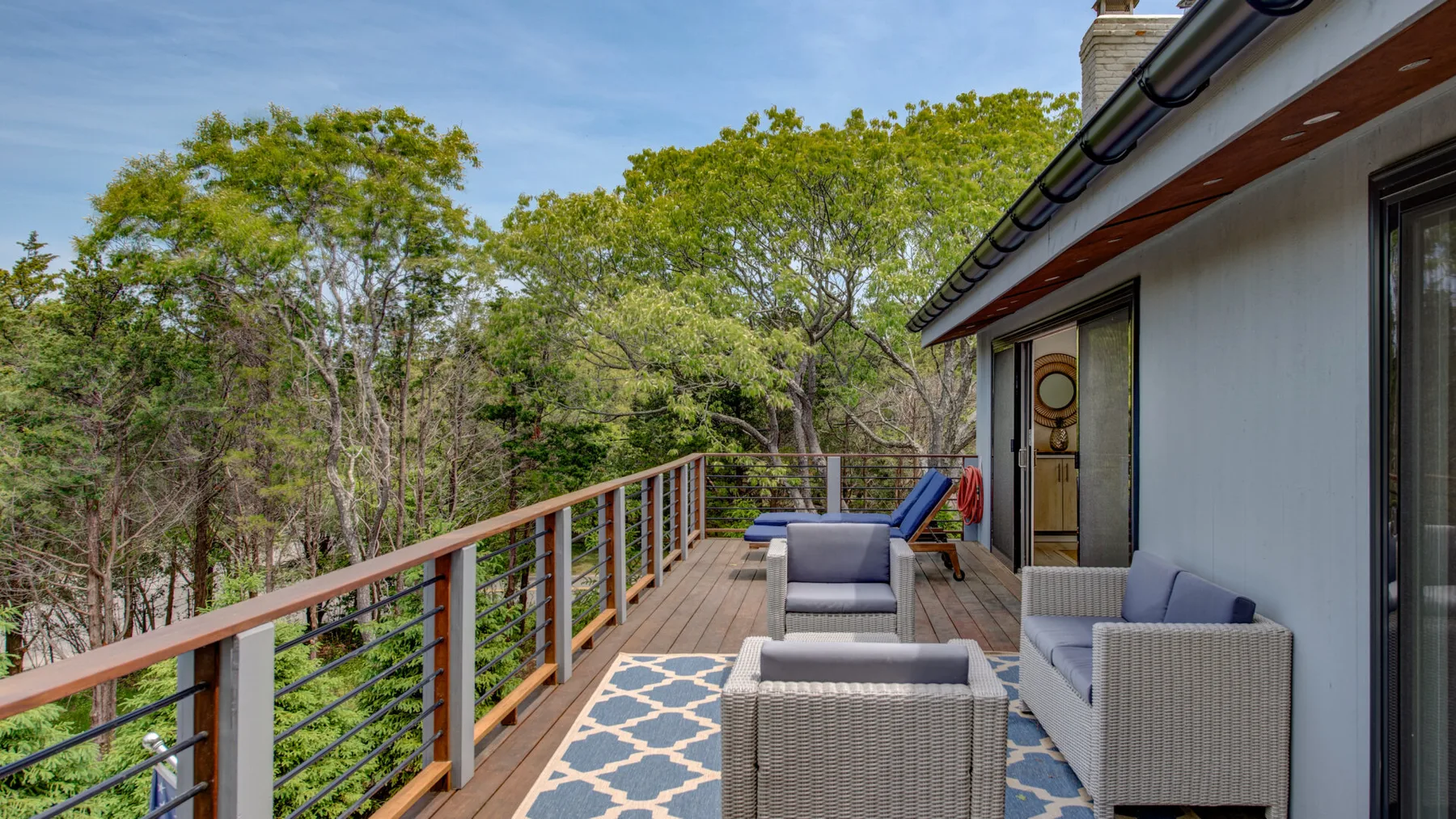 An outdoor deck has seating, a patterned rug, and a railing beside the house.