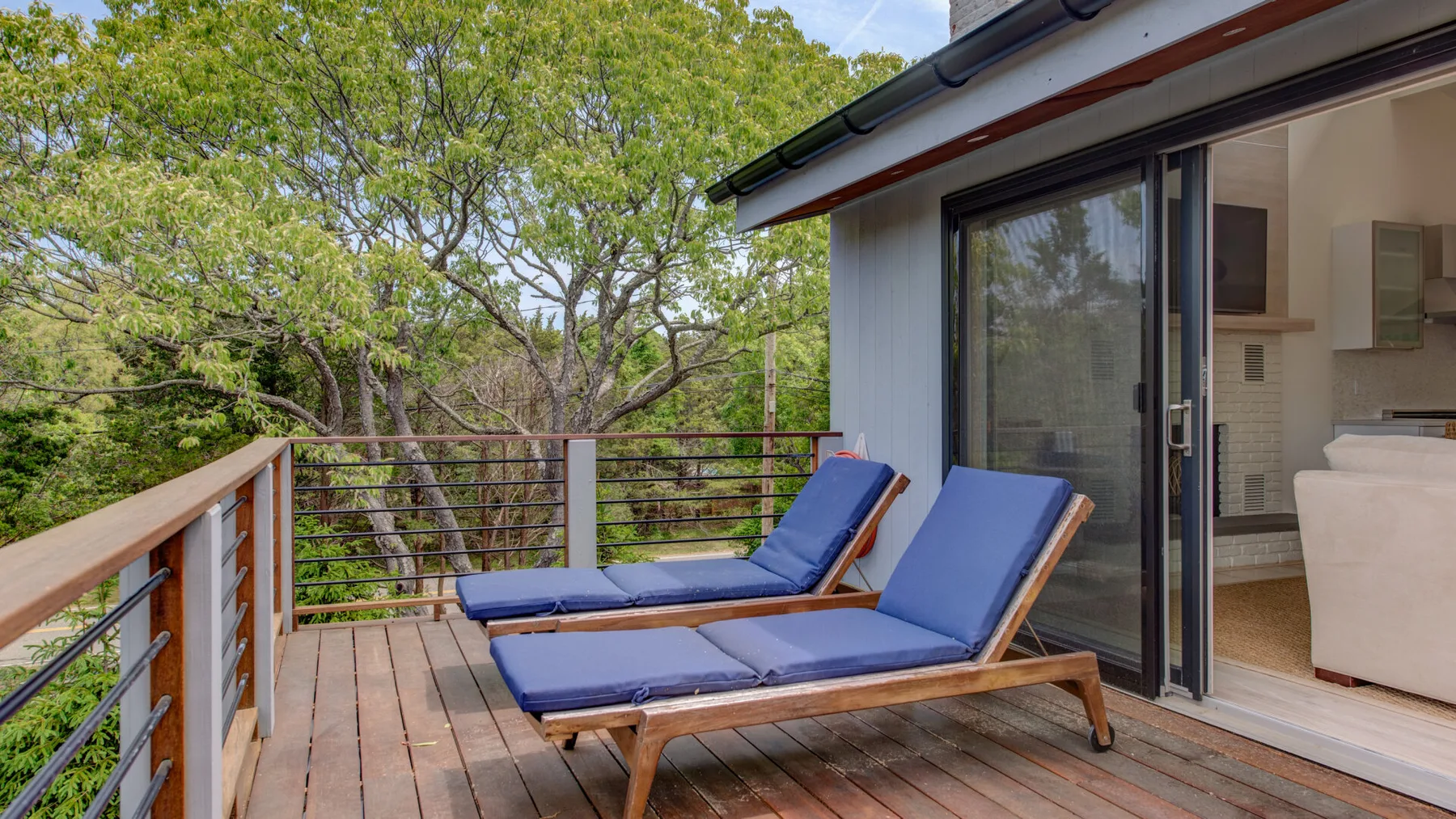 A wooden deck has two blue lounge seats beside an open sliding glass door.