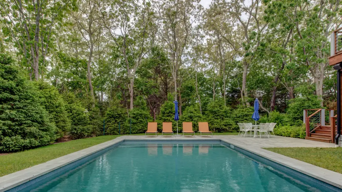 An outdoor swimming pool bordered by greenery, with patio seating at the far end.
