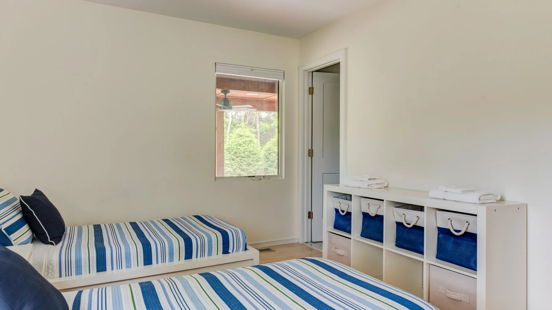 A bright bedroom with striped bedding and a window overlooking greenery.