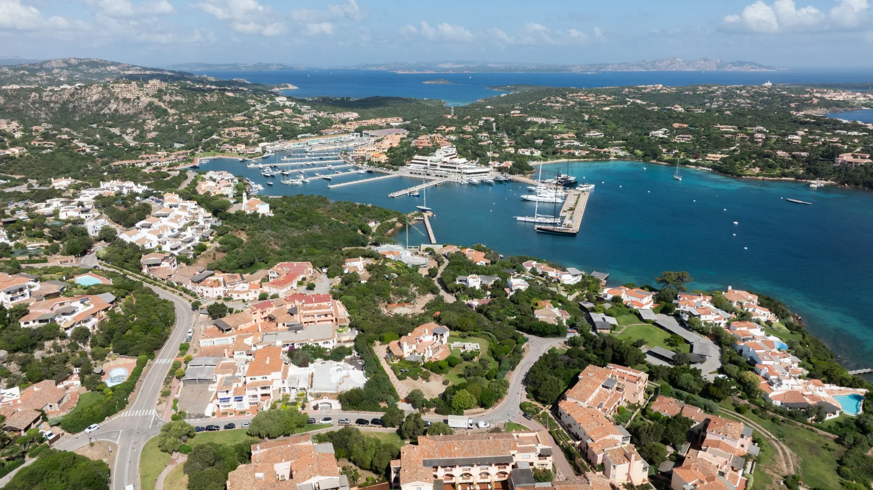 An aerial view of a coastal town, with boats in a blue-water harbor.