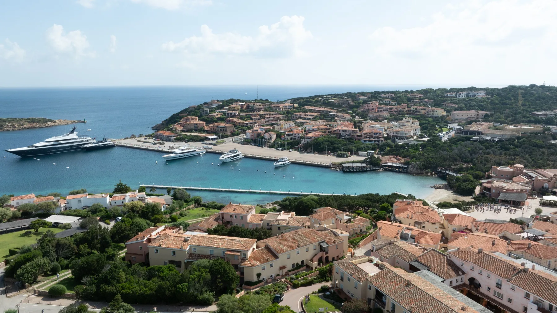 Aerial view of a coastal harbor with boats, waterfront buildings, and the sea.