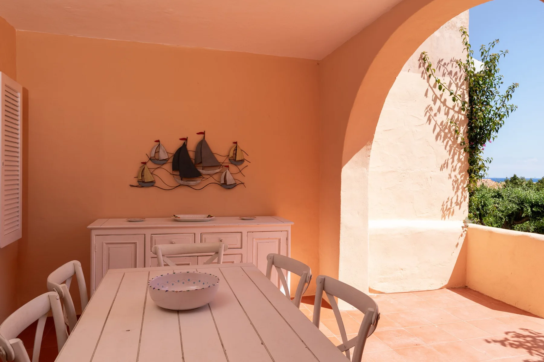 A peach-colored dining area opens through a large arch to an outdoor terrace.