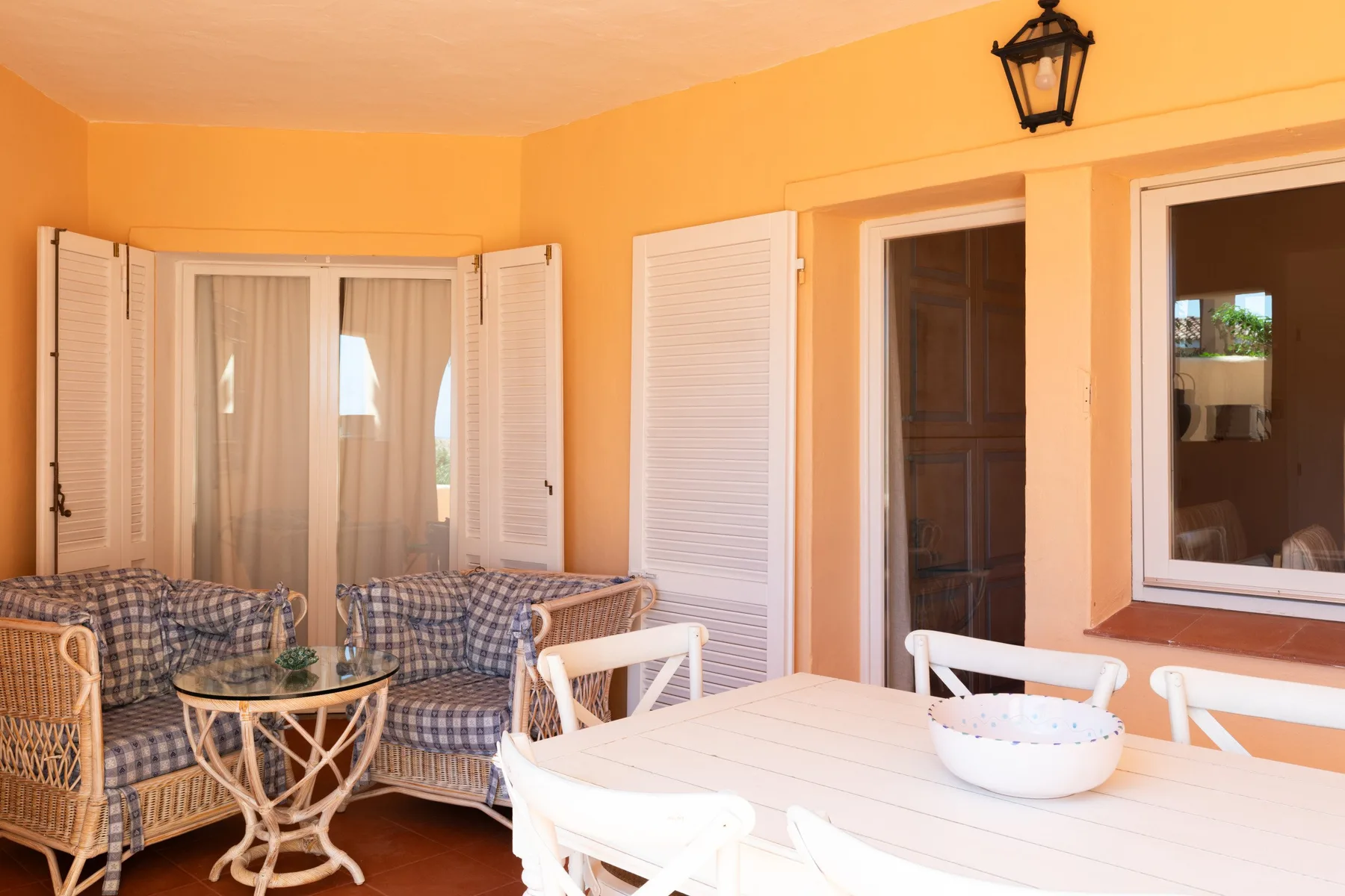 A furnished patio with a dining table and seating beside shuttered windows.
