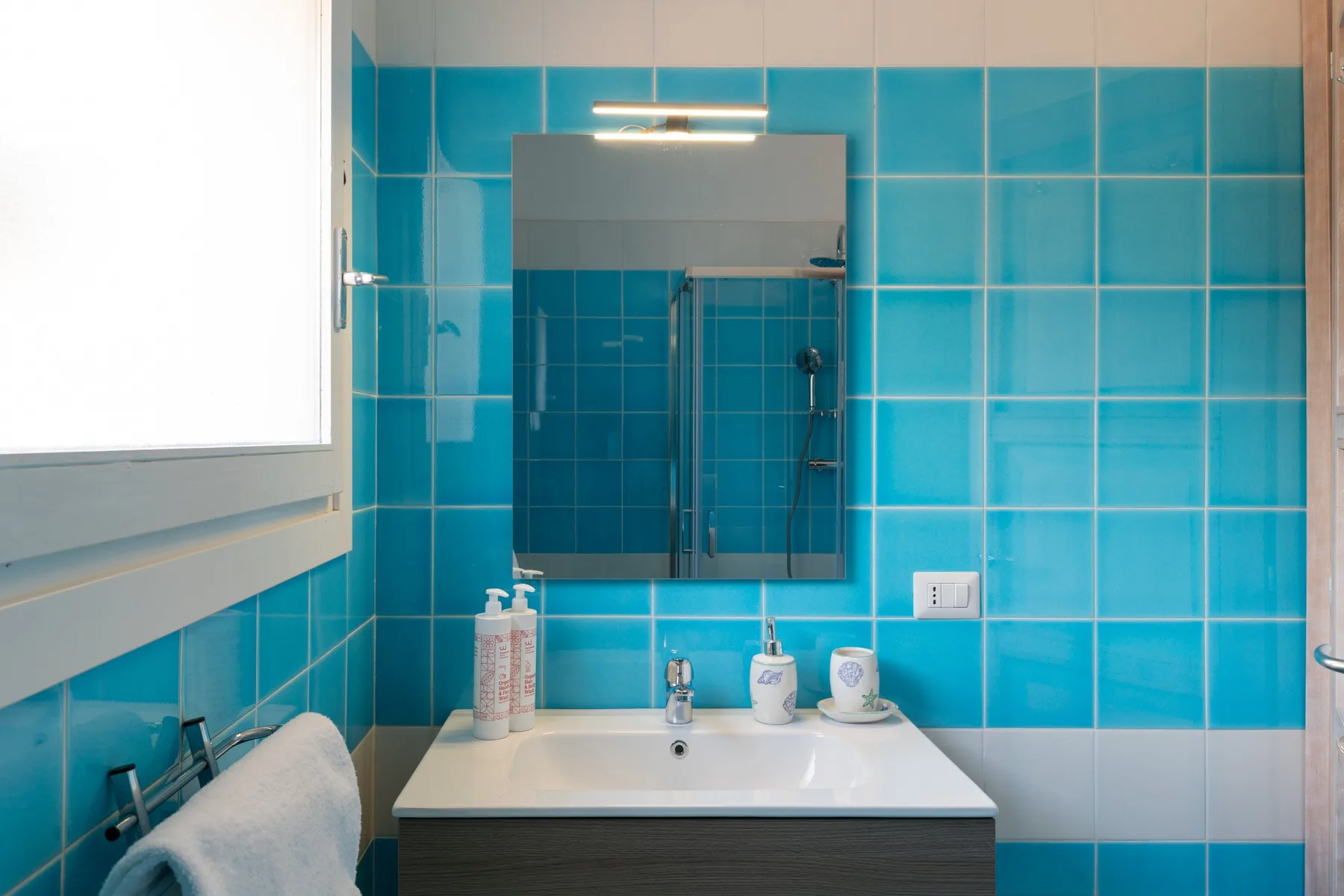 A bathroom vanity with a sink and mirror against bright blue tiled walls.