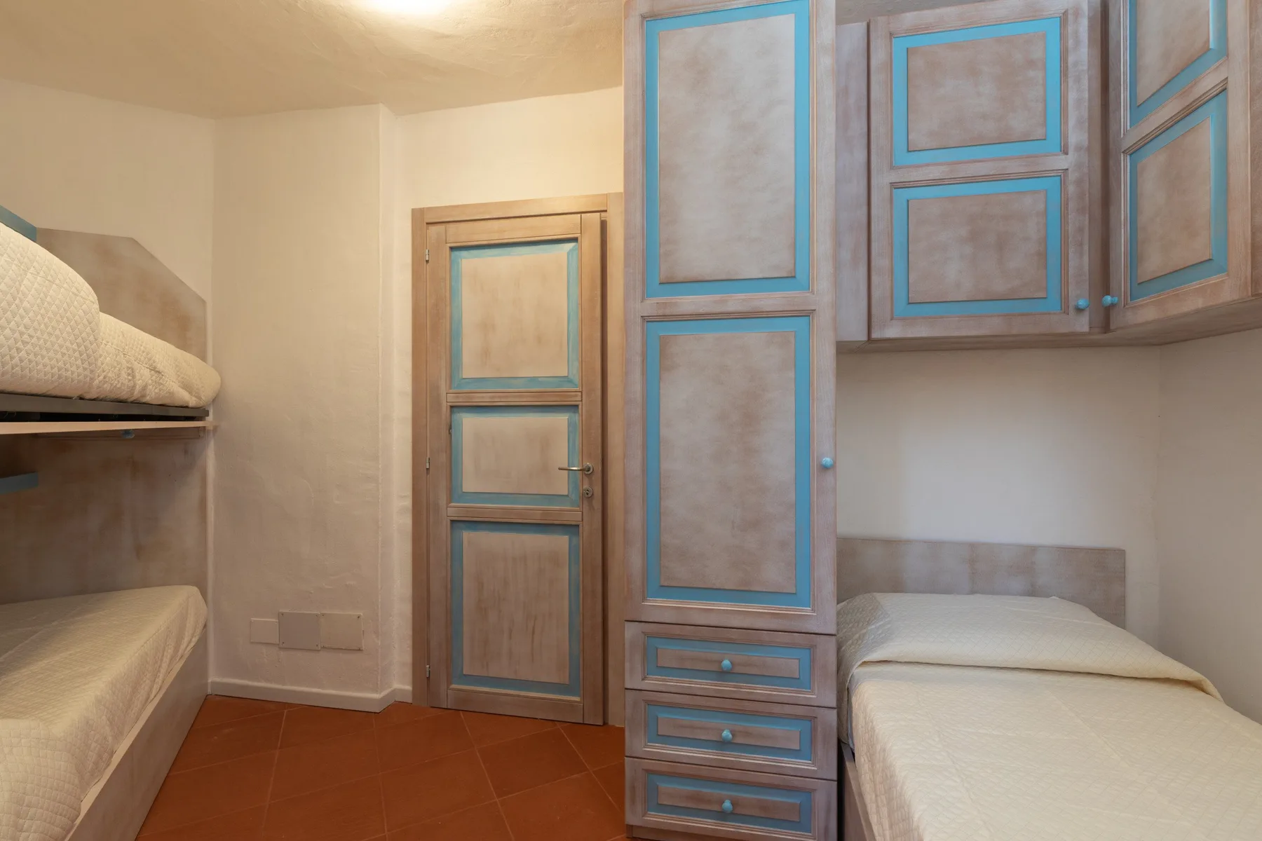 A compact bedroom with two beds and wooden storage cabinets.
