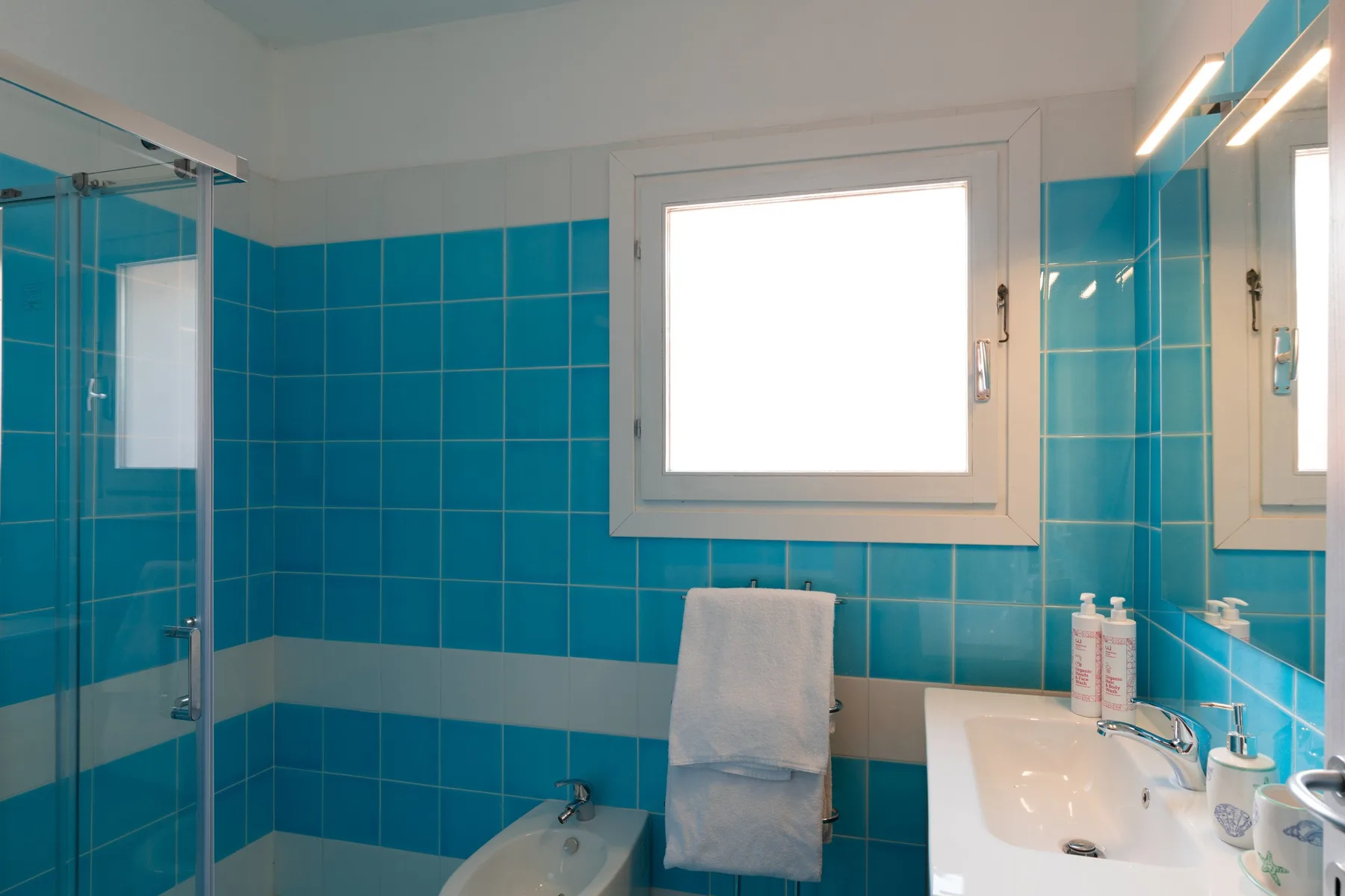 A tiled bathroom with a window, shower, and sink.