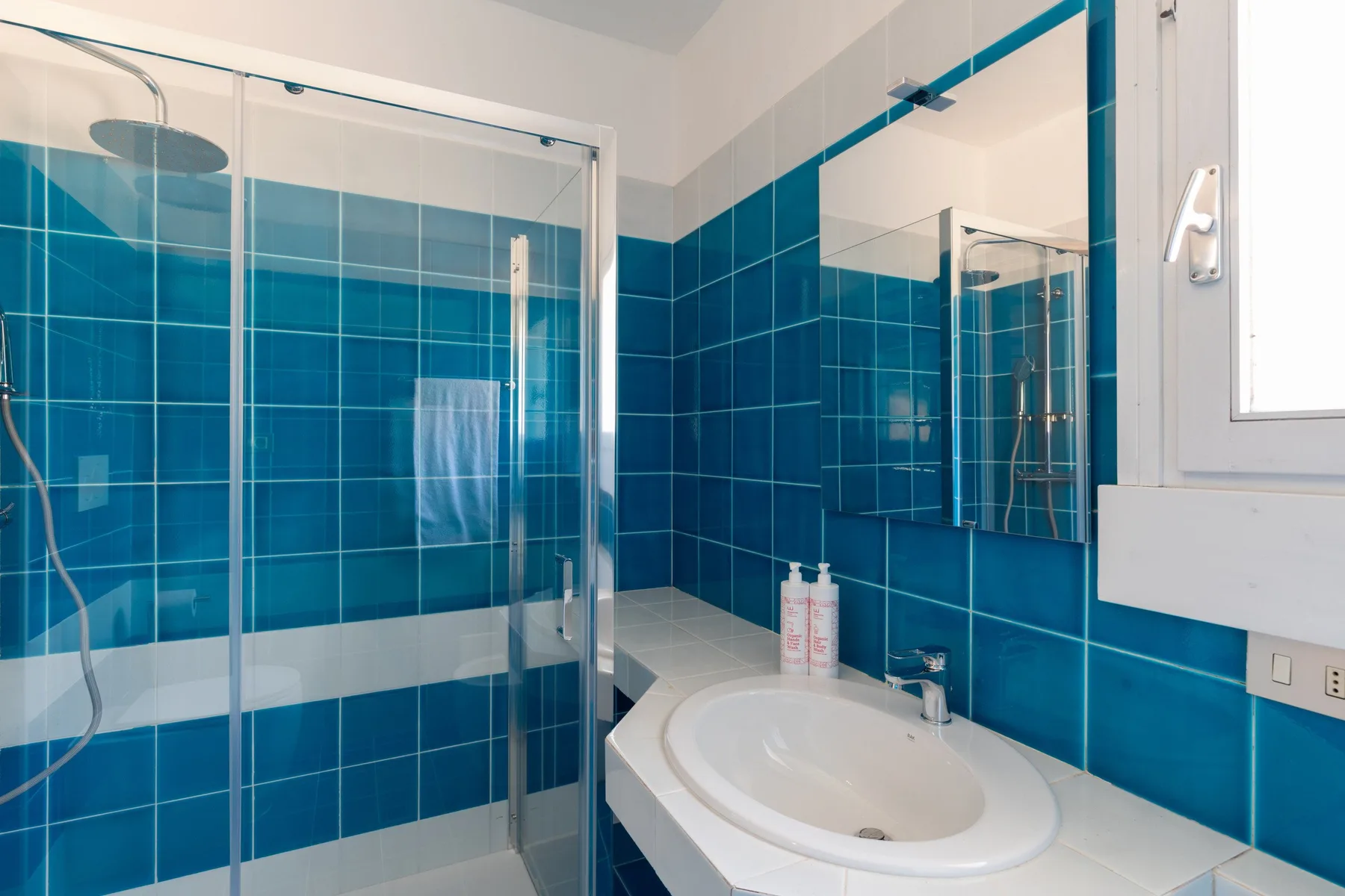 A bathroom with blue tiled walls, a glass shower, and a sink.