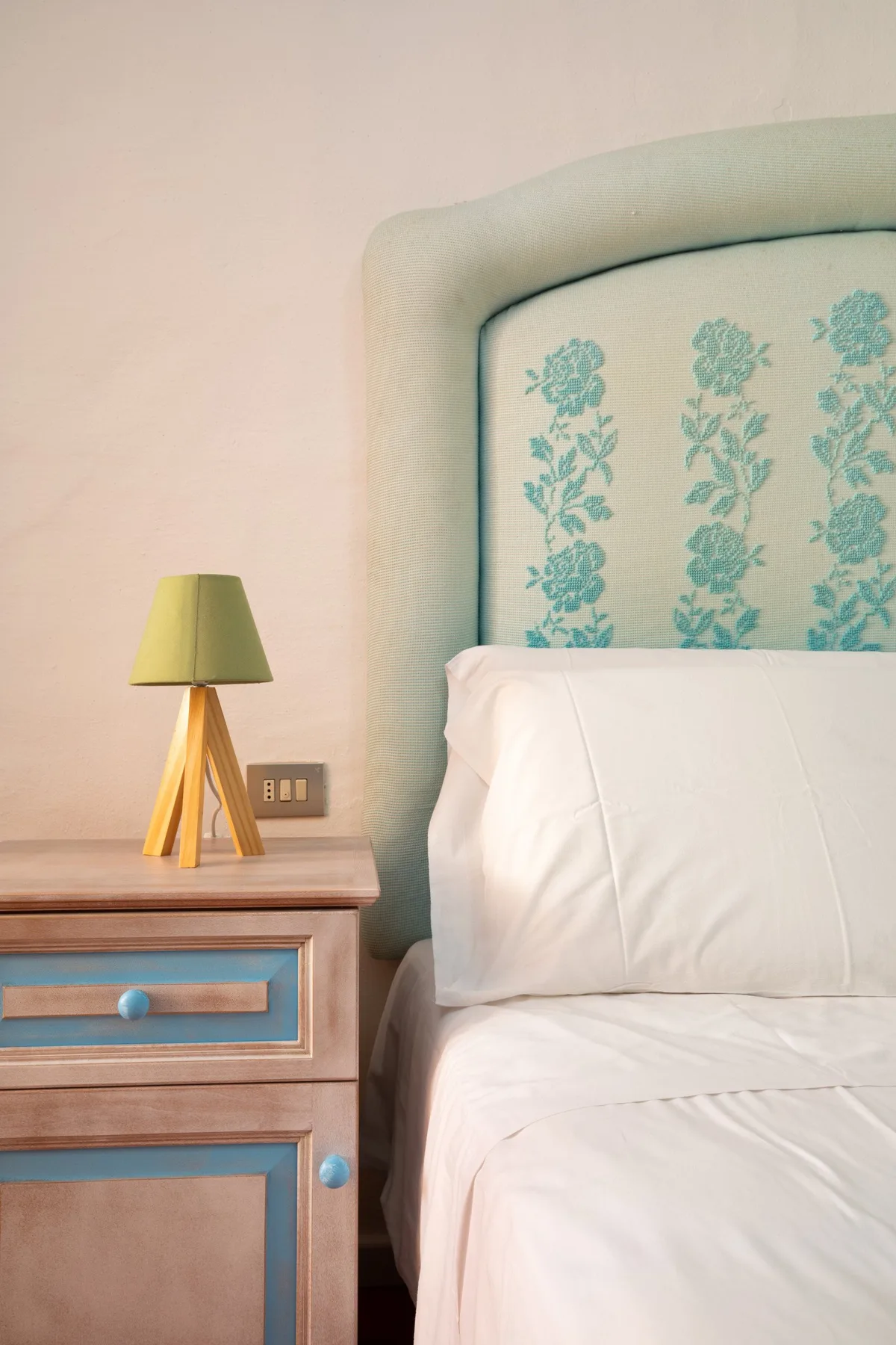 A bedroom with a bed, patterned upholstered headboard, and bedside table with a lamp.