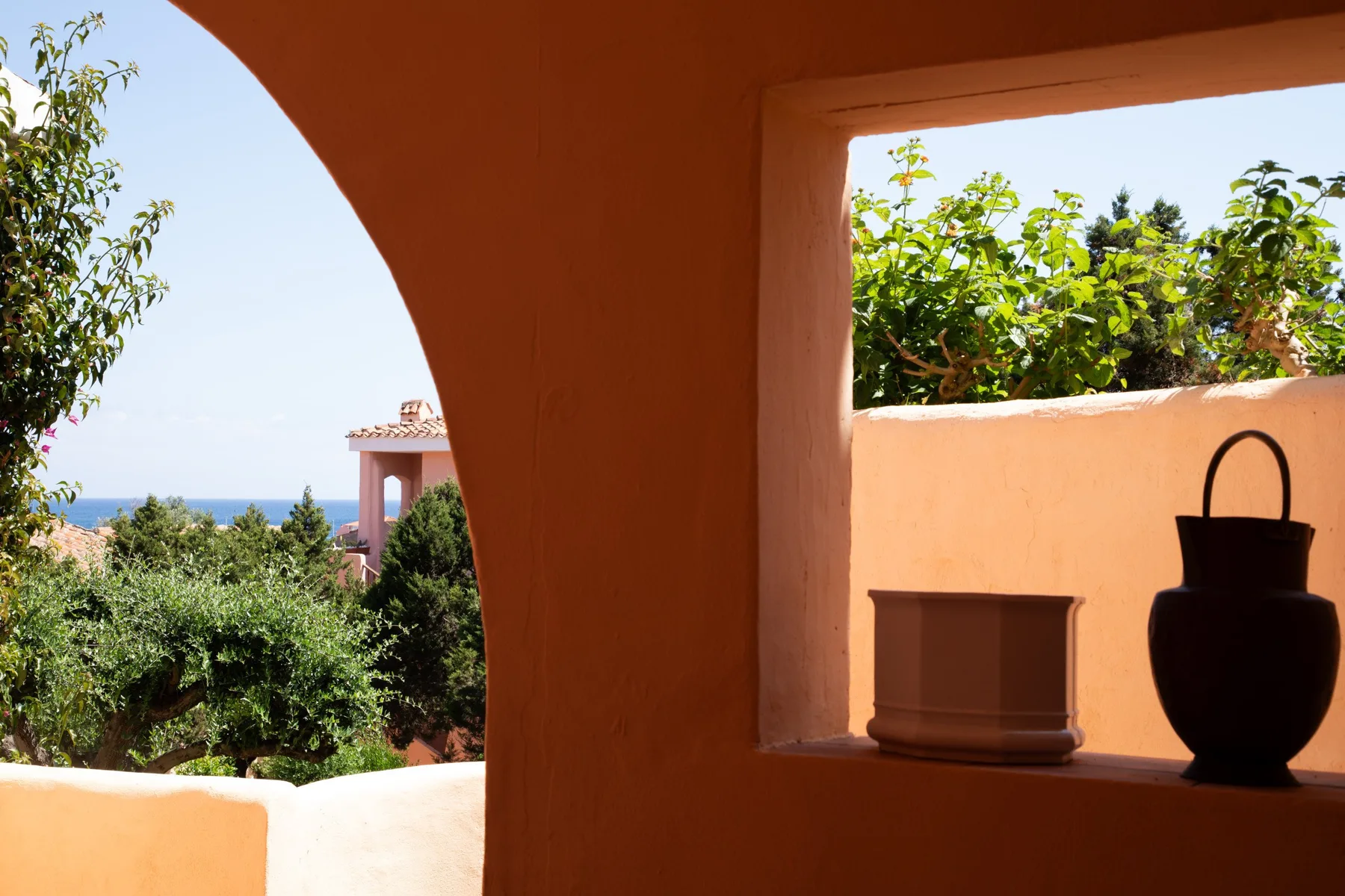 A sunlit terracotta archway frames a garden and distant sea view.