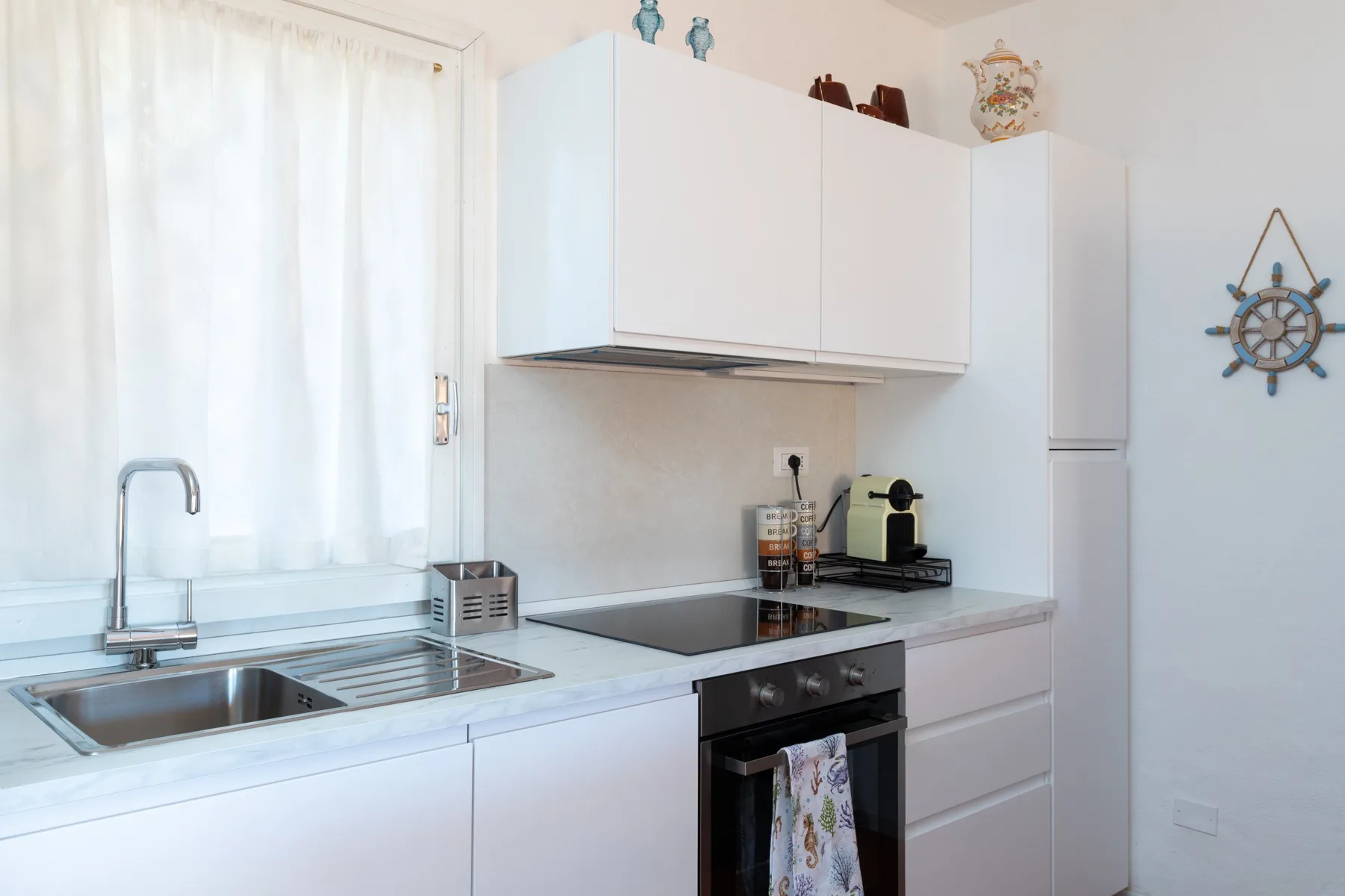 A bright kitchen with white cabinets, a sink, and a stovetop.