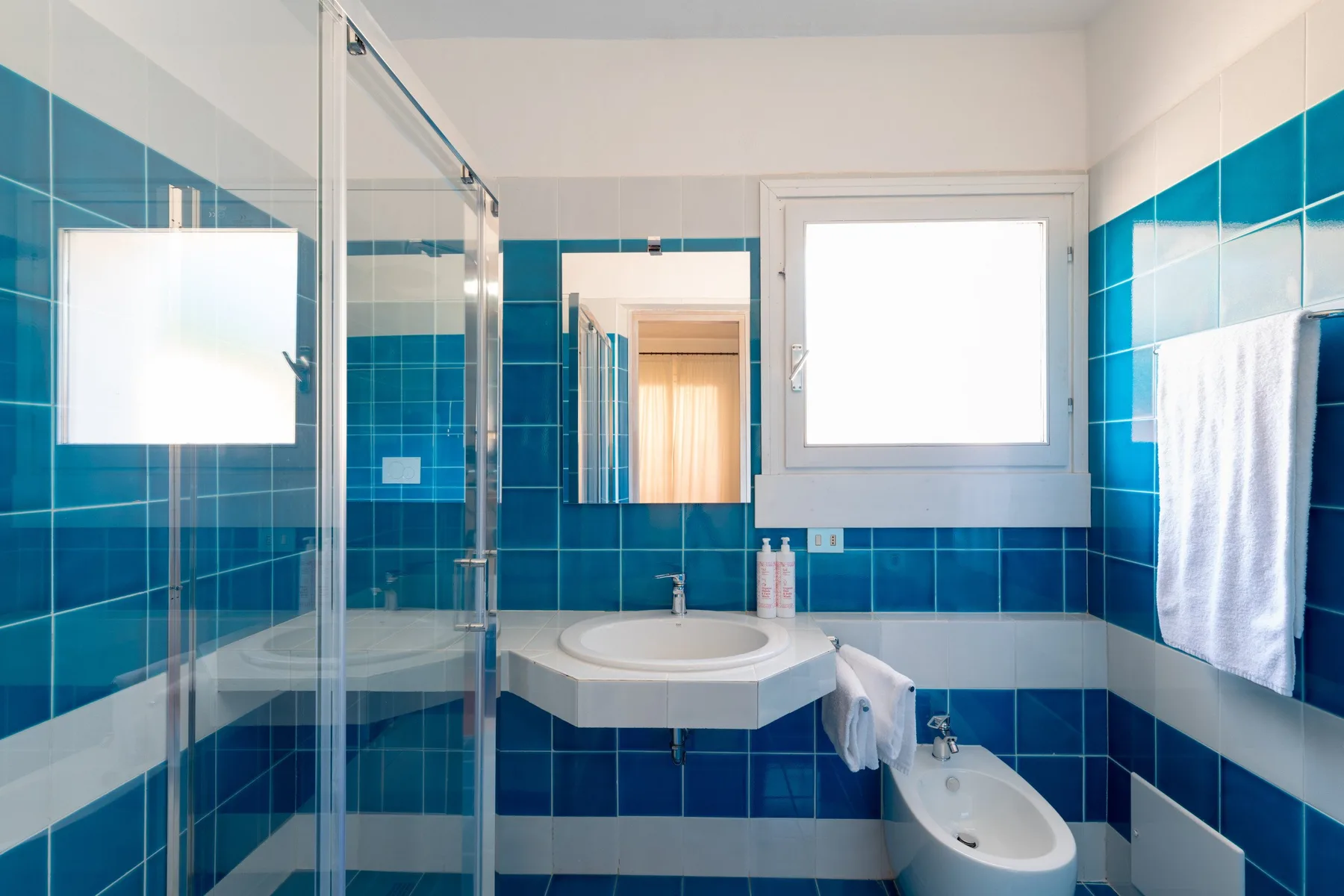 A tiled bathroom with a glass shower, sink, and toilet.