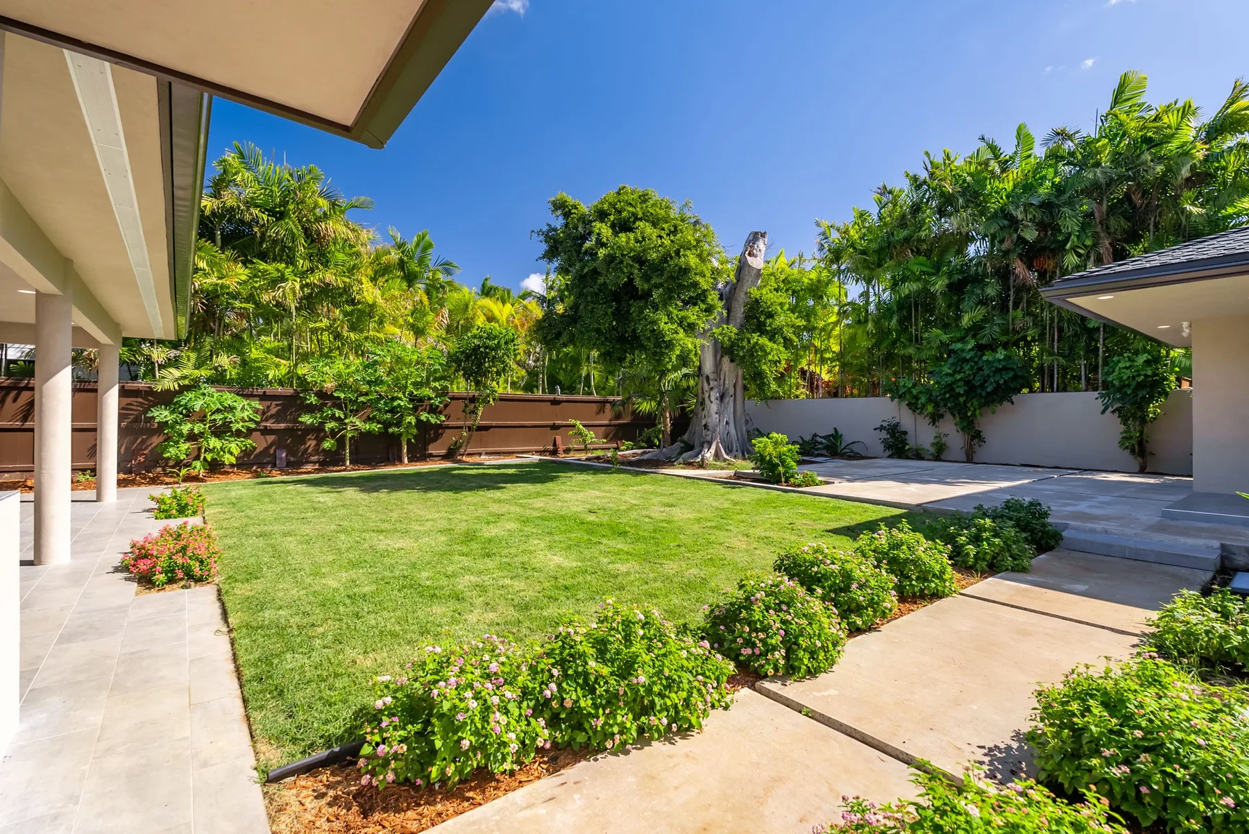 A landscaped garden with a lawn, flowering shrubs, and a paved walkway.