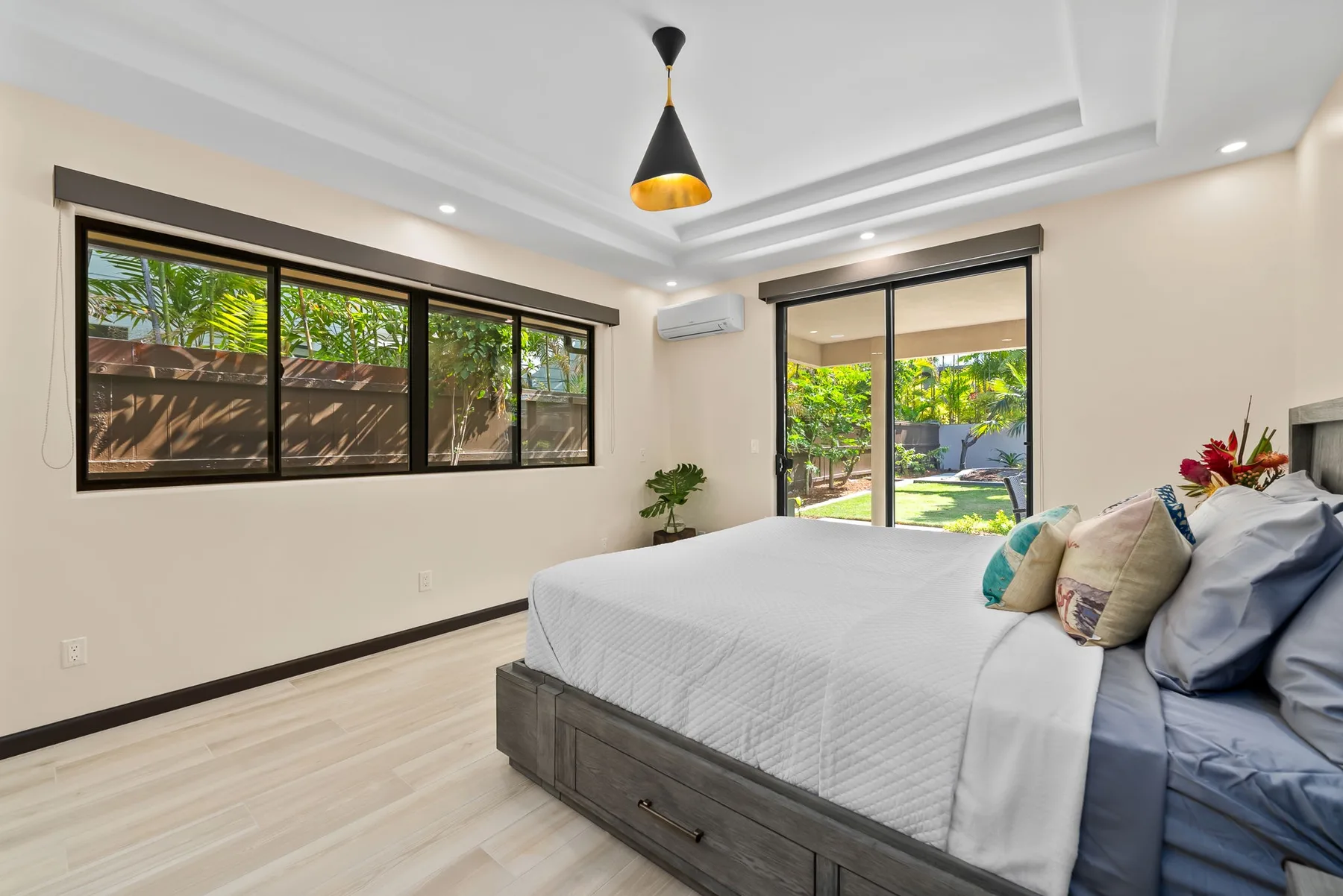 A bright bedroom with a bed beside large windows overlooking a garden.