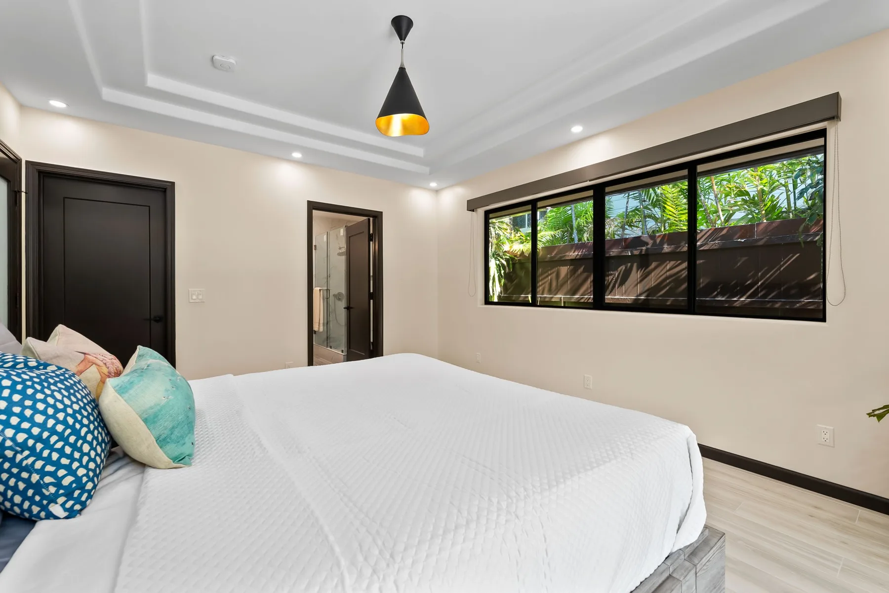 A bedroom with a large bed and a wide window overlooking greenery.