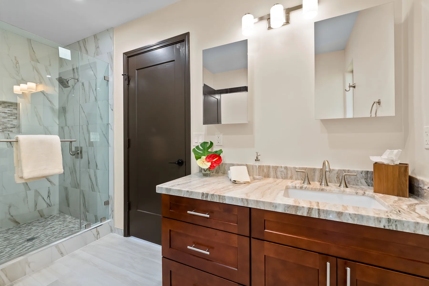 A bathroom vanity with a sink and mirror sits beside a glass shower.