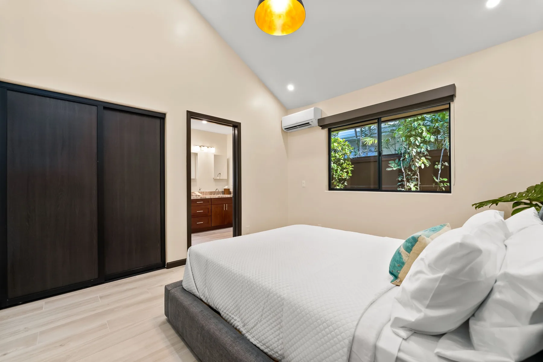 A bedroom with a neatly made bed and a window overlooking greenery.