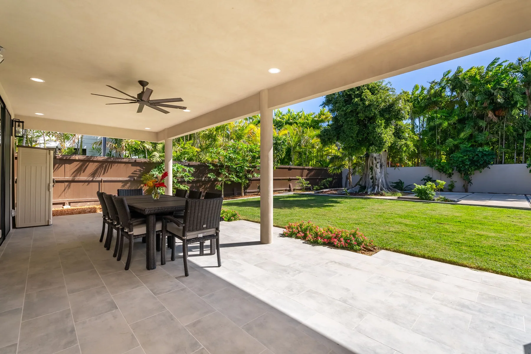 A covered outdoor dining area opens onto a green lawn and garden.