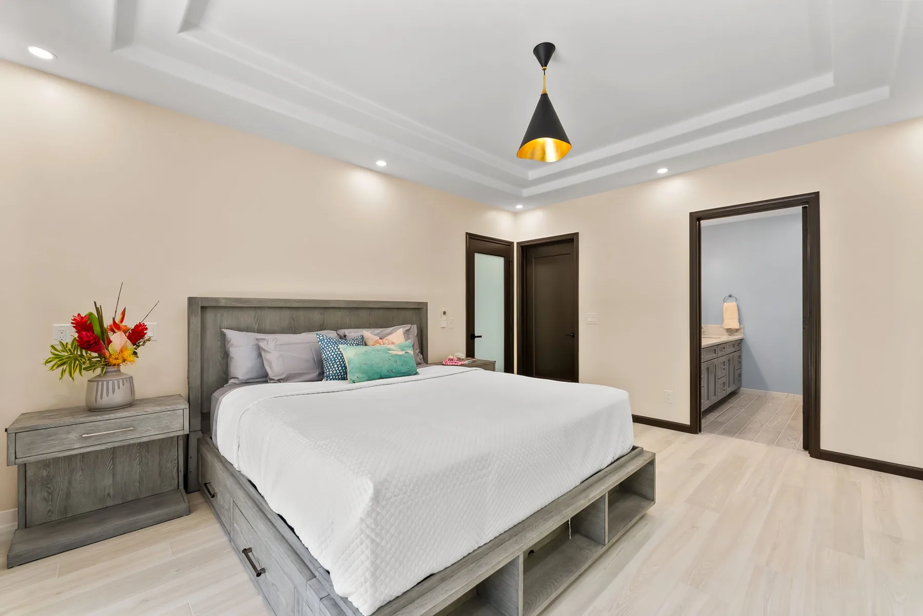 A bedroom with a neatly made bed and a bedside table with flowers.
